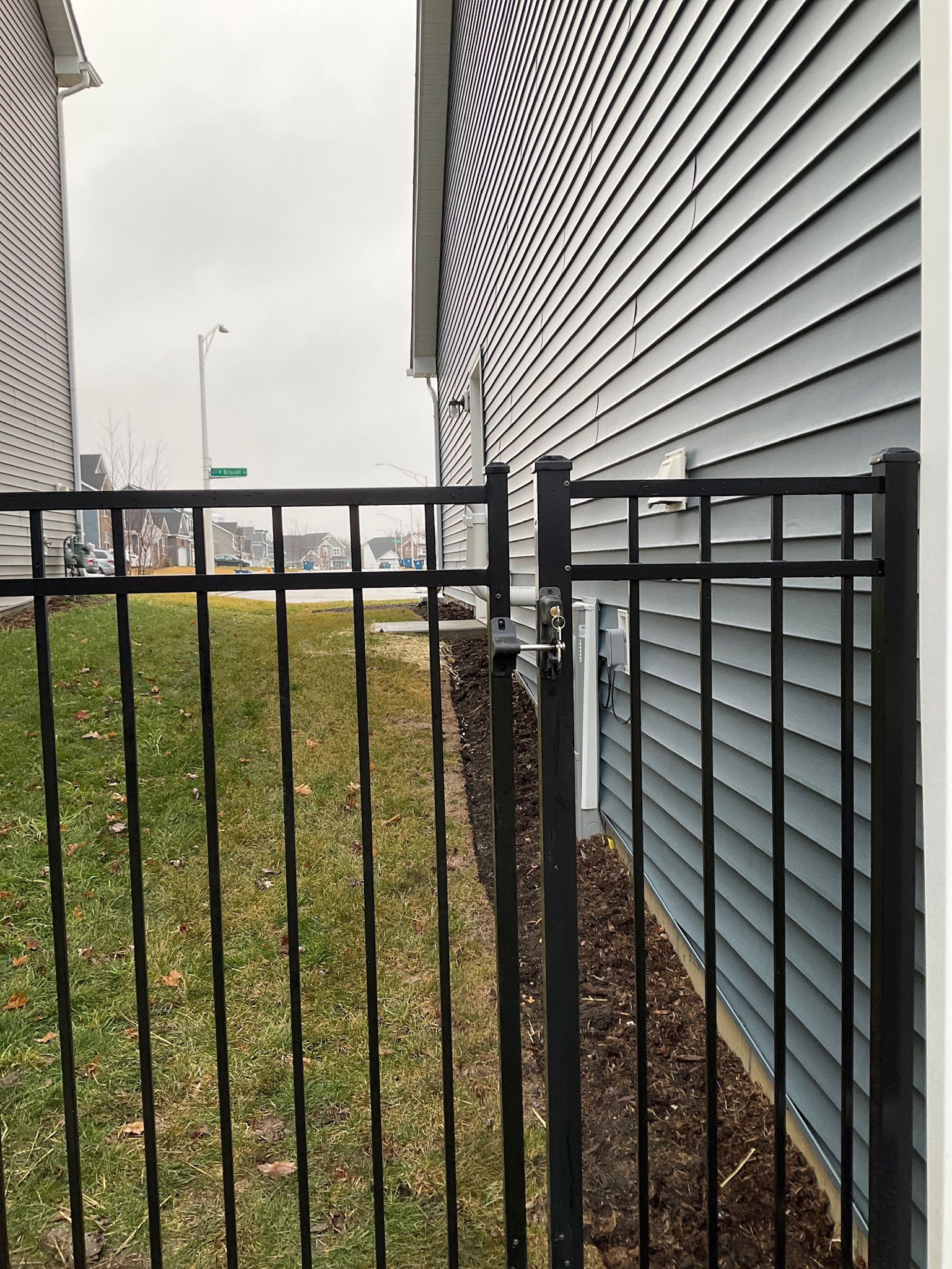 Black metal fence next to a house with blue siding. Overcast day.
