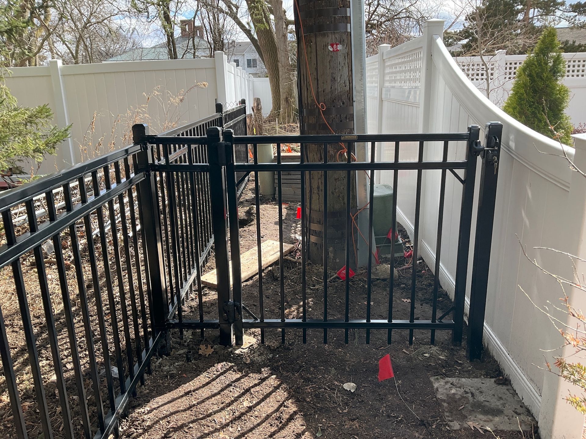 Black metal fence surrounds a tree. White fence on either side. Brown ground.