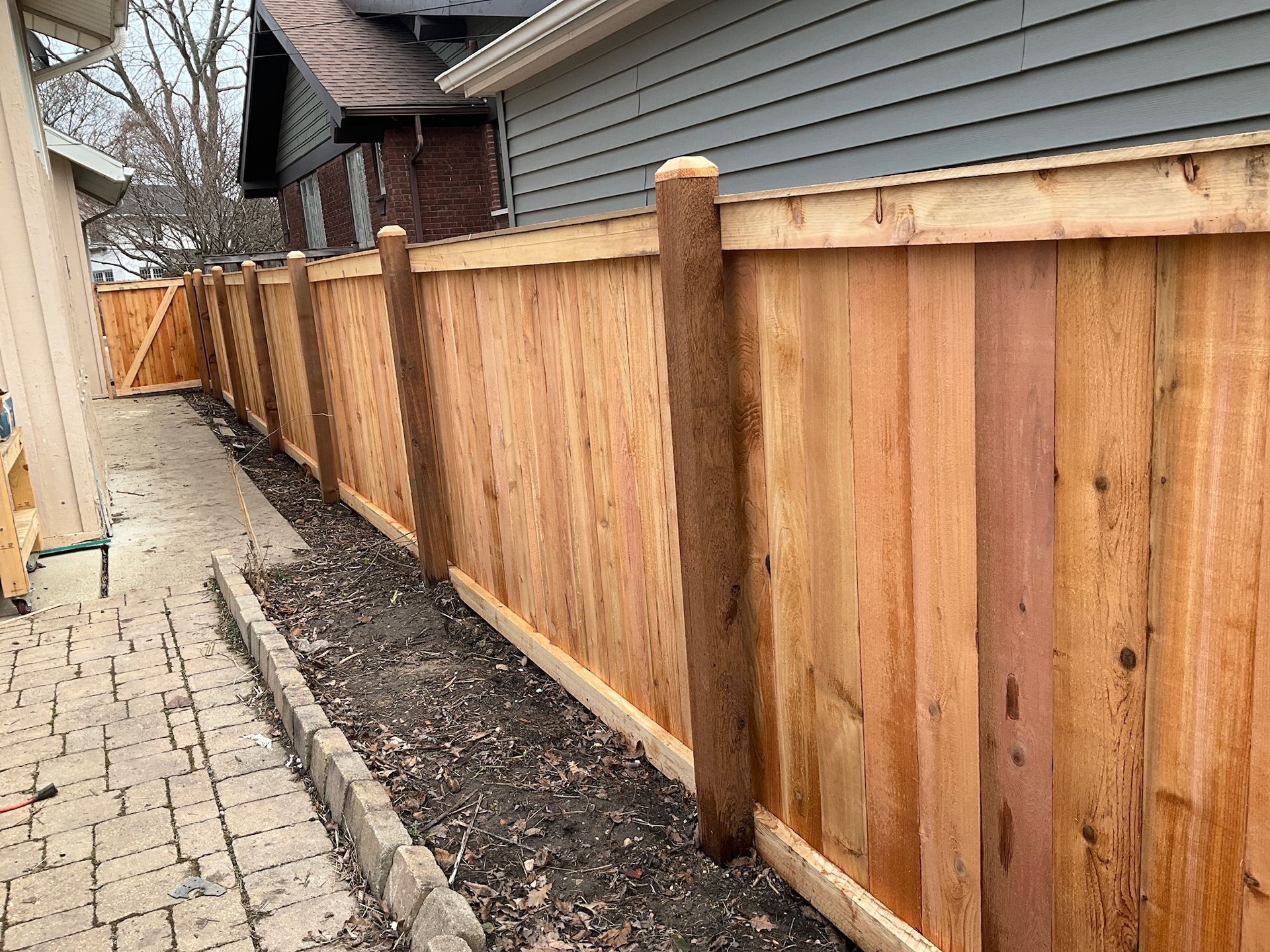 Wooden fence bordering a narrow dirt path and a paved walkway.