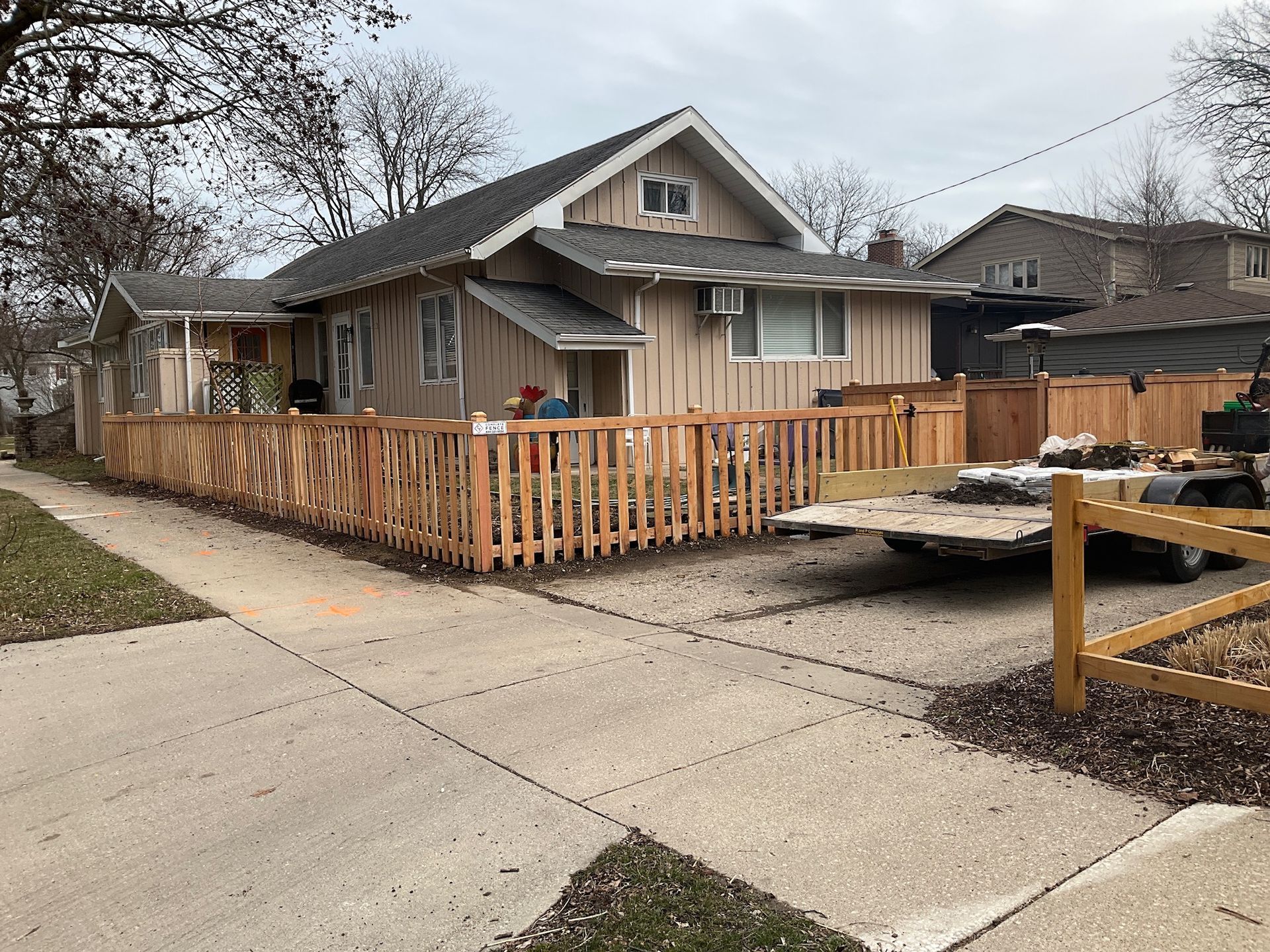 Tan house with new wooden fence and a trailer in the driveway.
