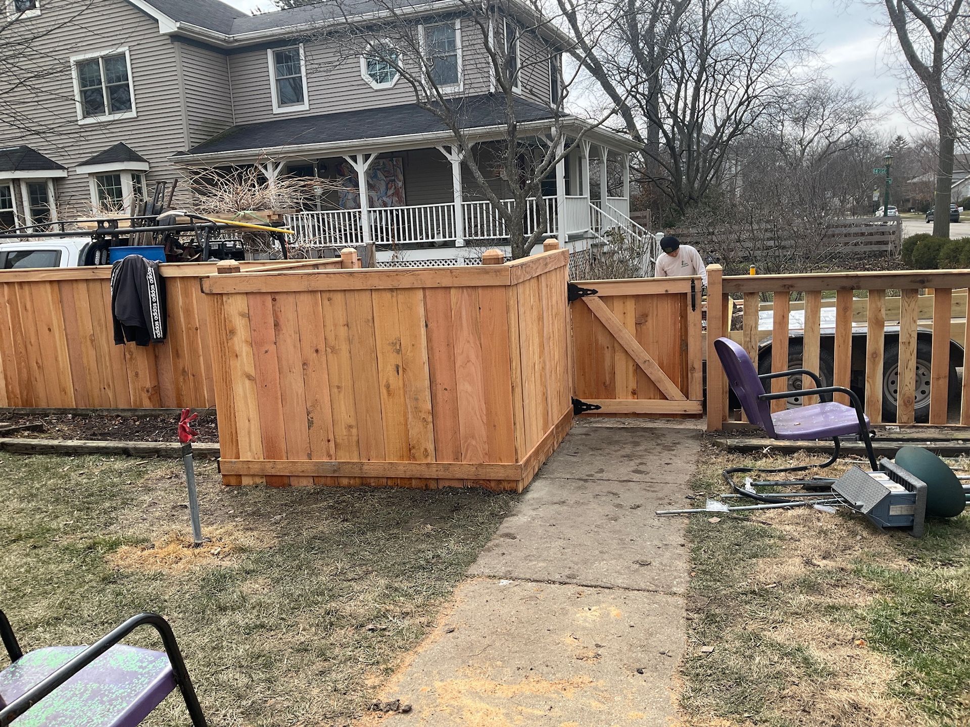 A wooden fence with a gate in front of a house. Person standing near the gate. Cloudy day.