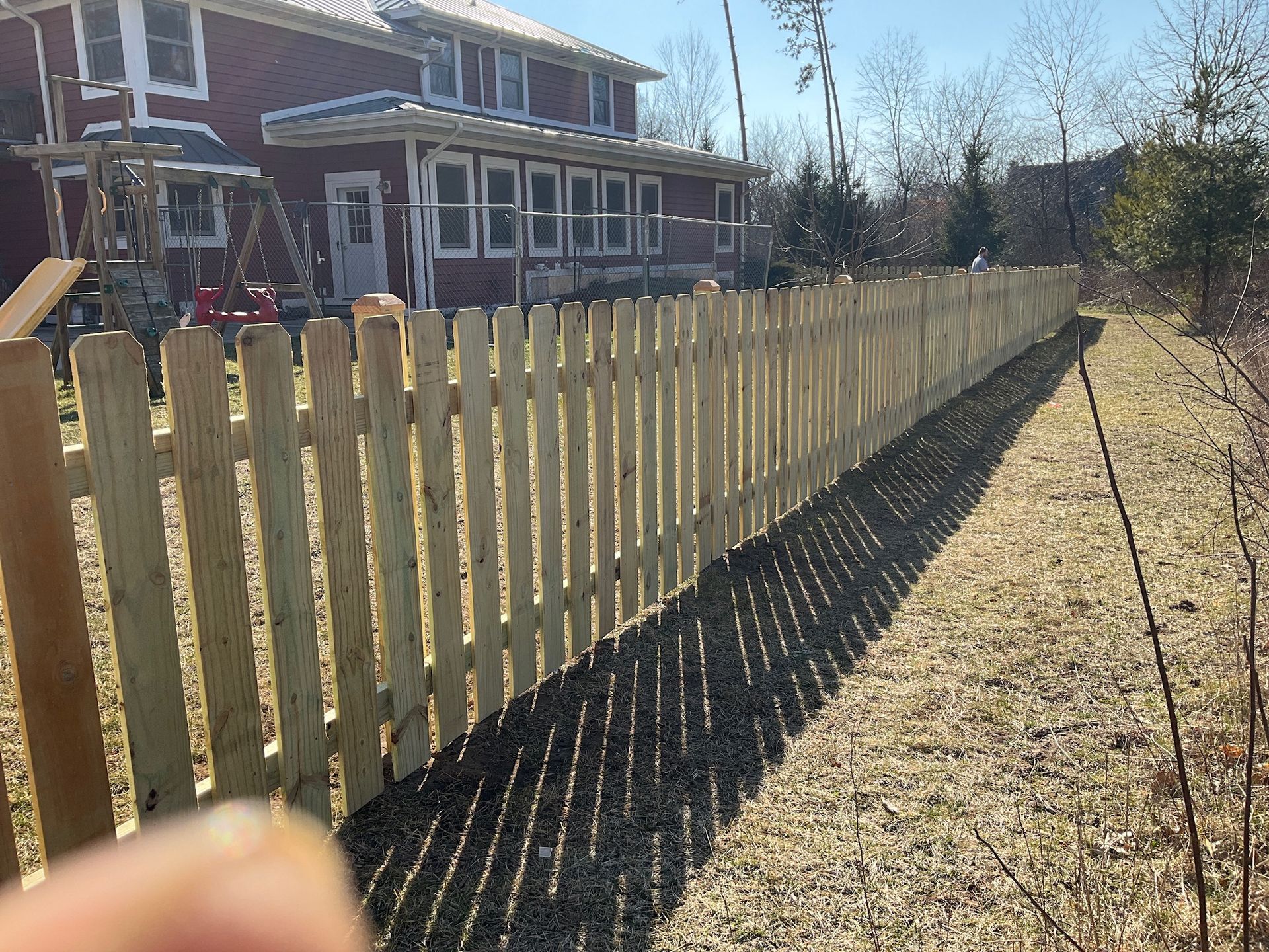 Wooden picket fence in front of a brick house on a sunny day.