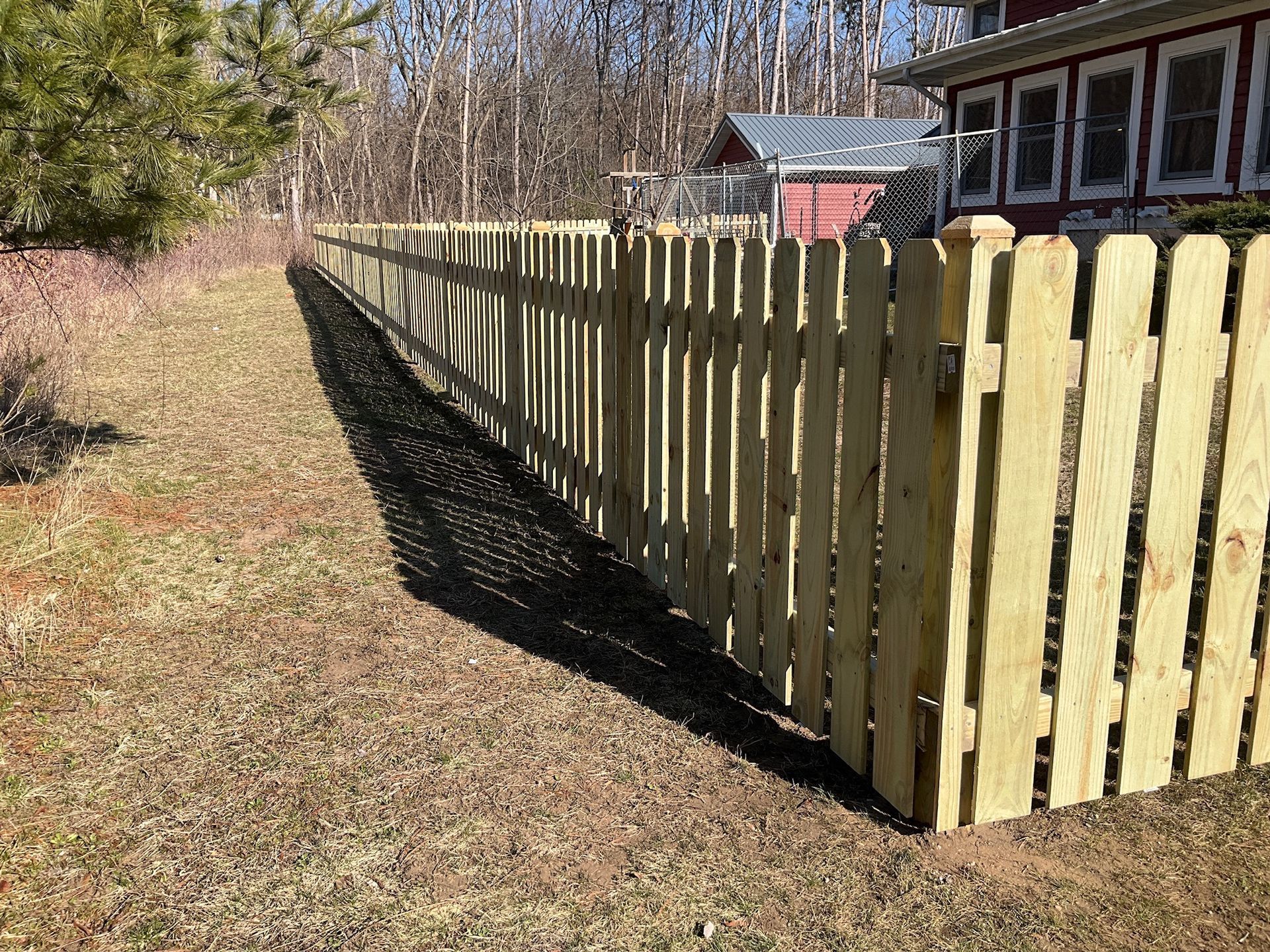 Wooden fence in a grassy yard, with a building and trees in the background on a sunny day.