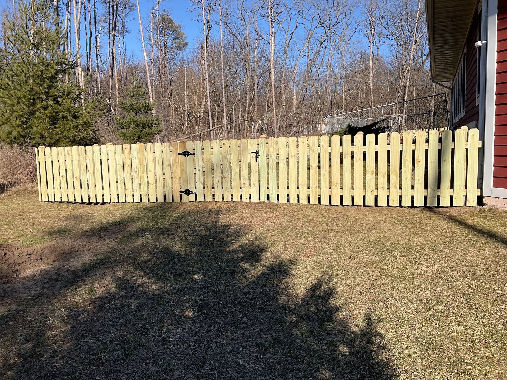 Wooden picket fence in a yard with a house and trees in the background.