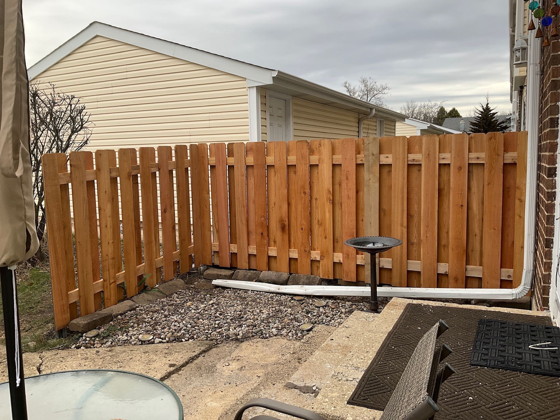Wooden fence in a yard with gravel, a bird bath, and a beige house in the background.