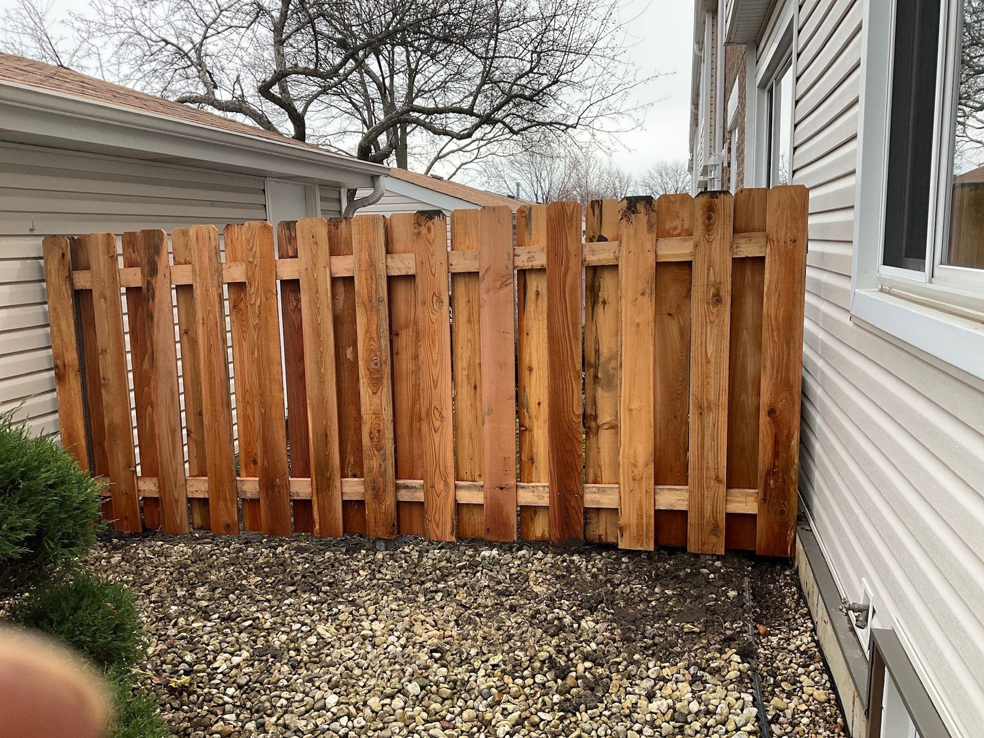 Wooden fence between two buildings in a yard covered in gravel.