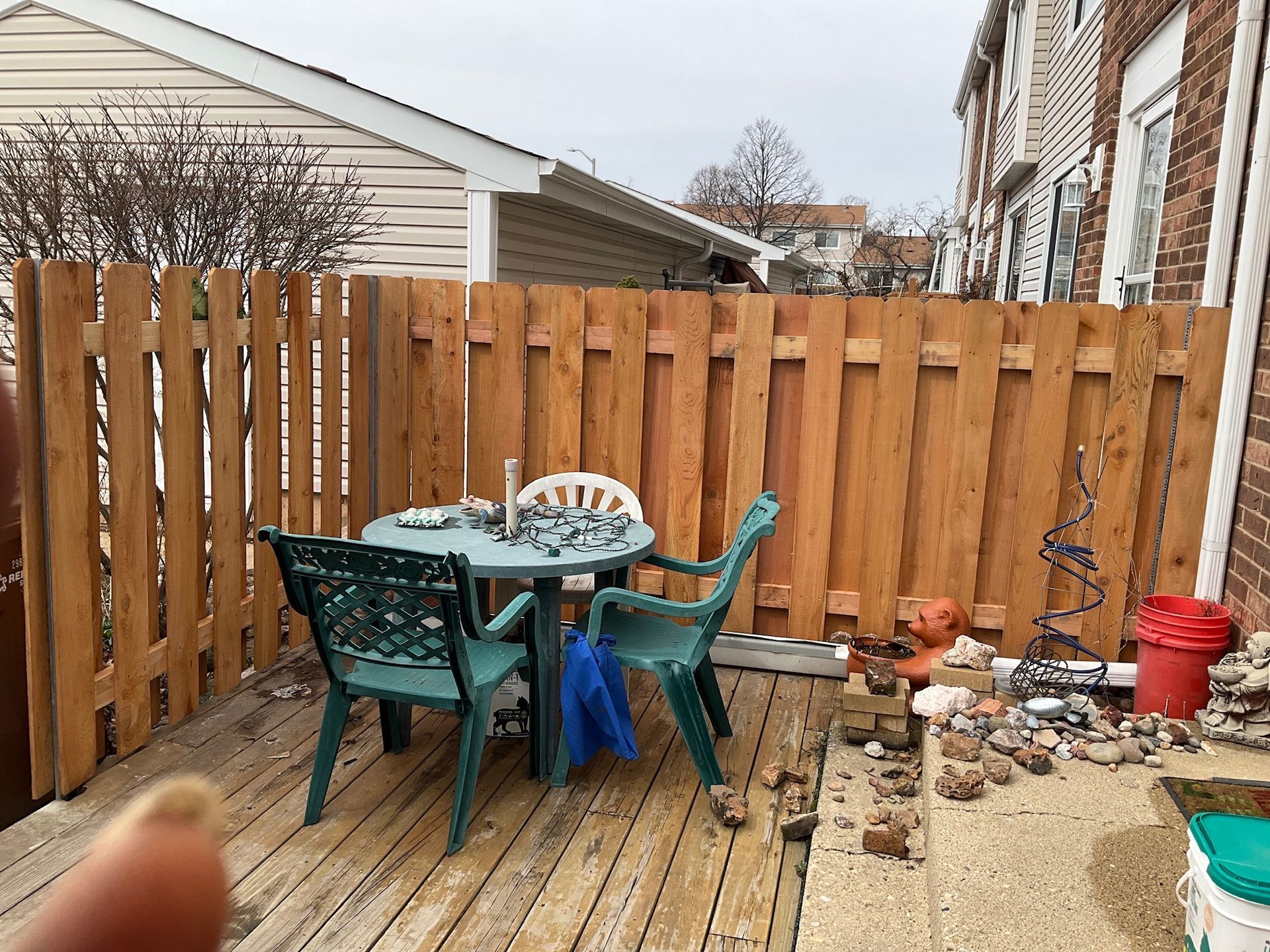 Wooden fenced-in backyard patio with a small table and two green chairs.