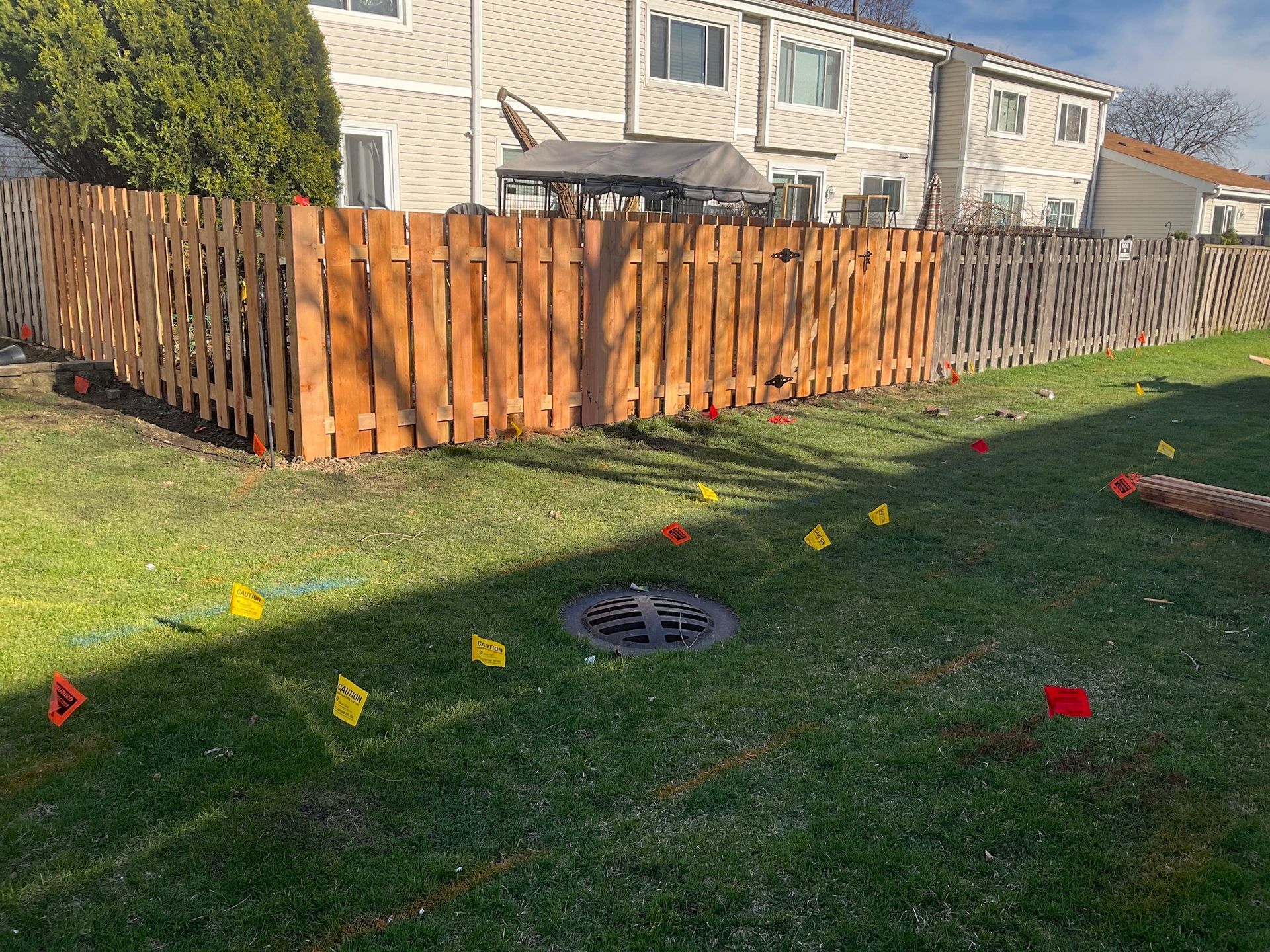 Wooden fence in a backyard with flags marking utility lines.