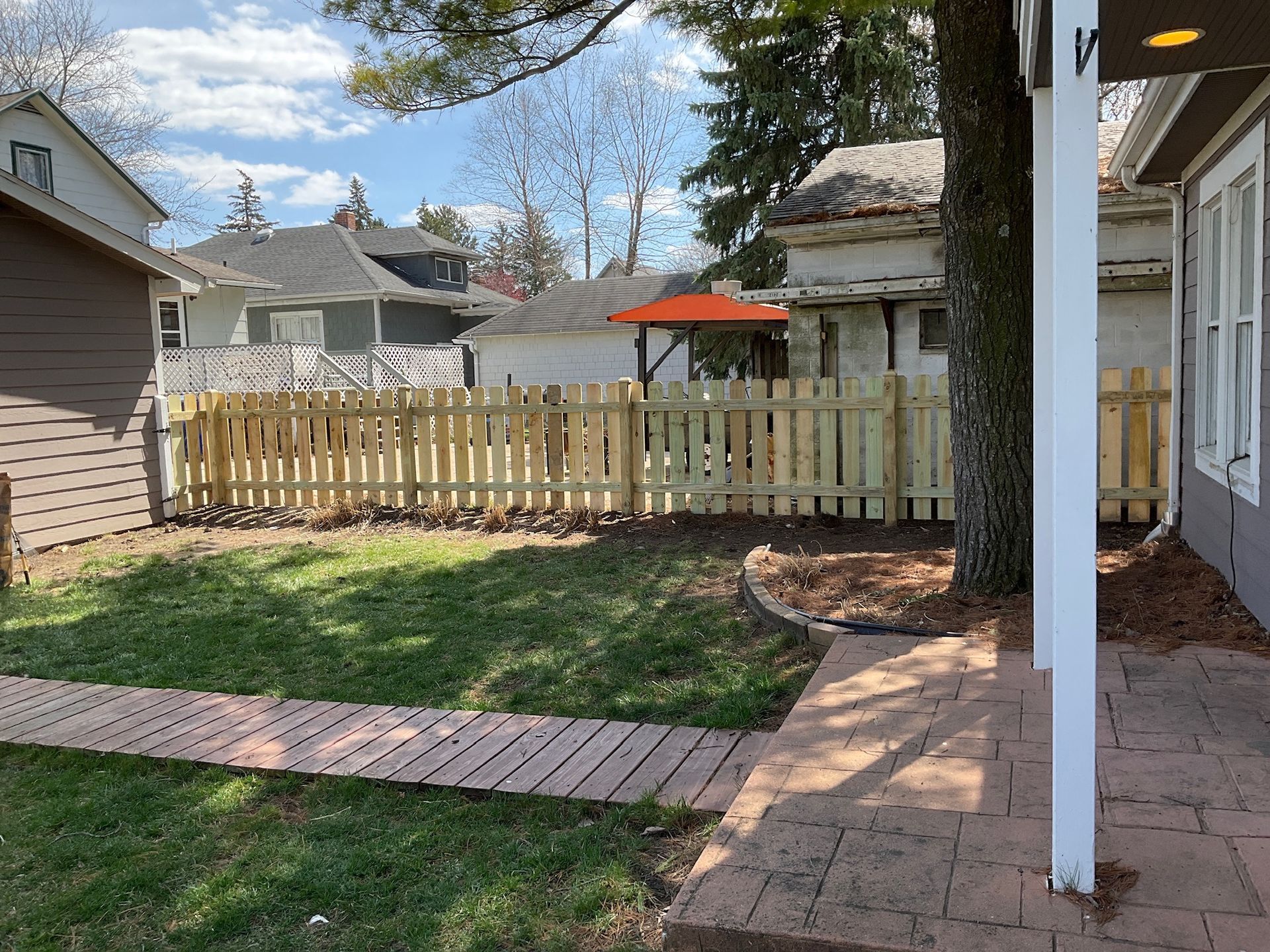 Backyard with a wooden fence, lawn, brick path, and small building.