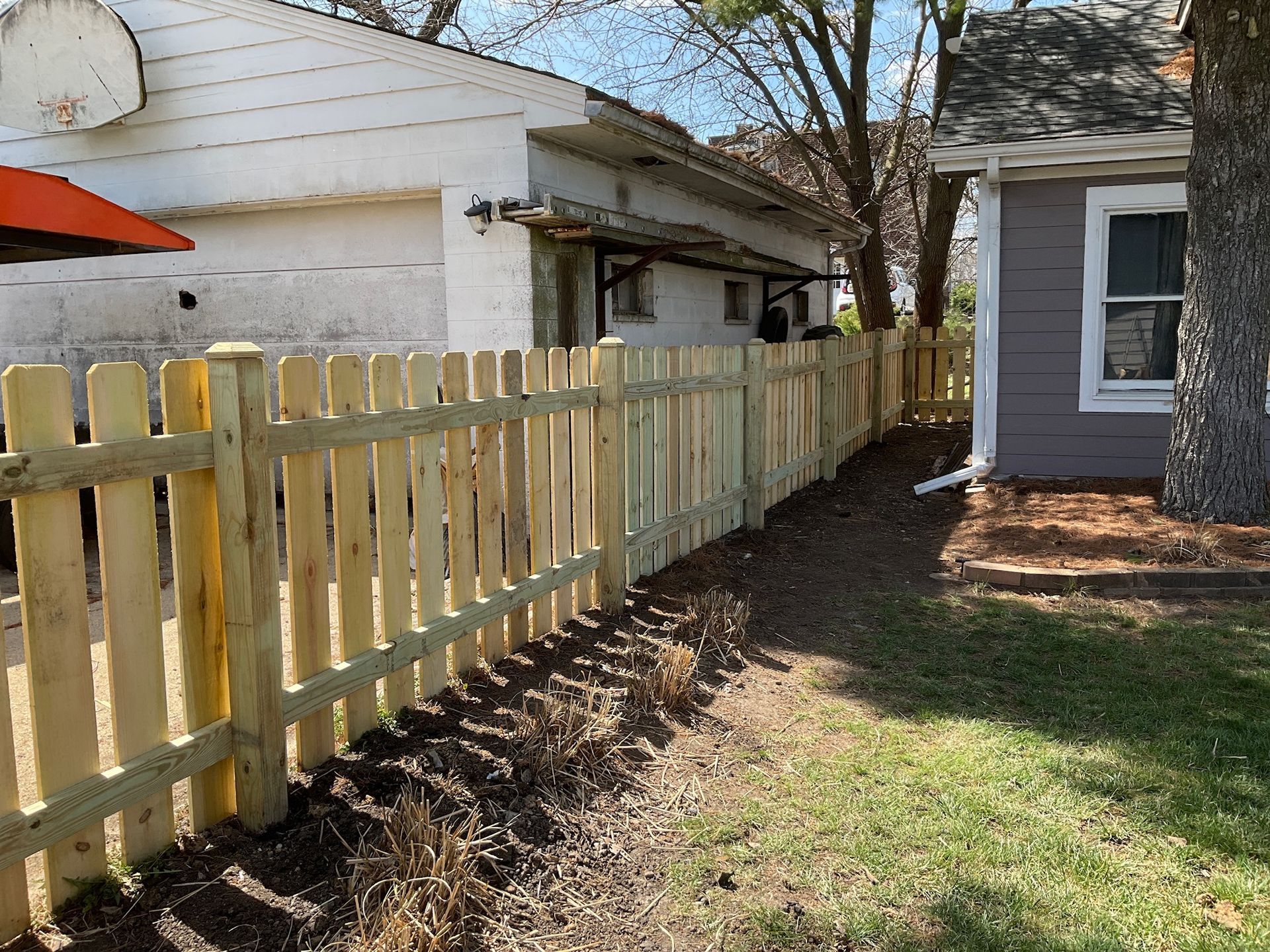 Wooden picket fence in a backyard, beside a house and garage, on a sunny day.