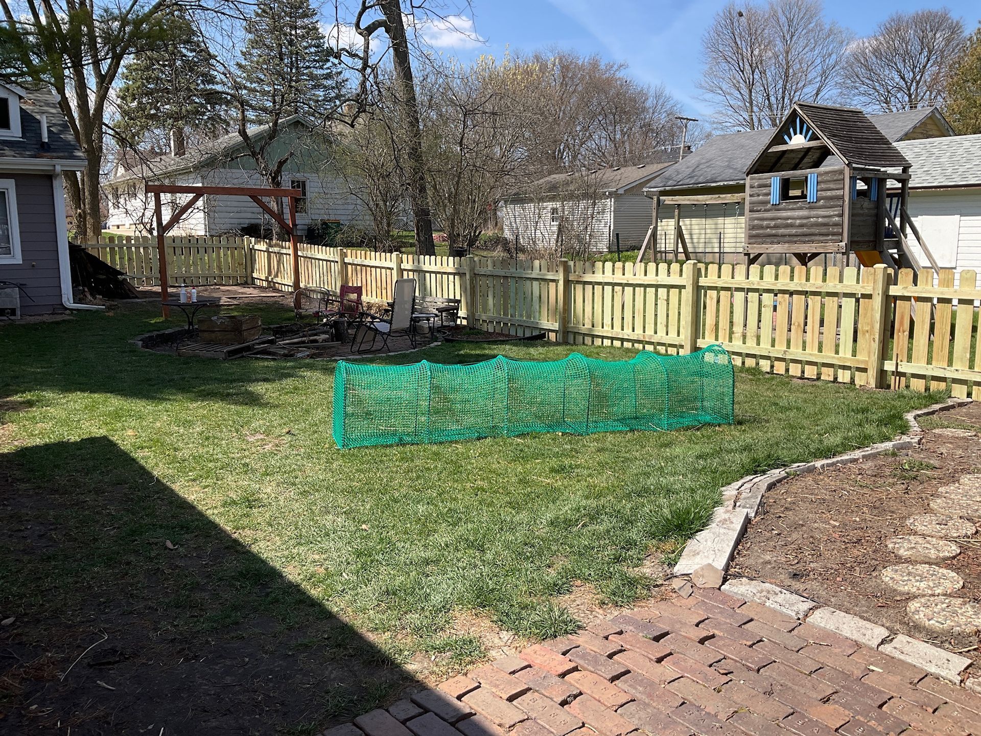 Backyard with a green lawn, wooden fence, a small playhouse, and a green mesh garden barrier.