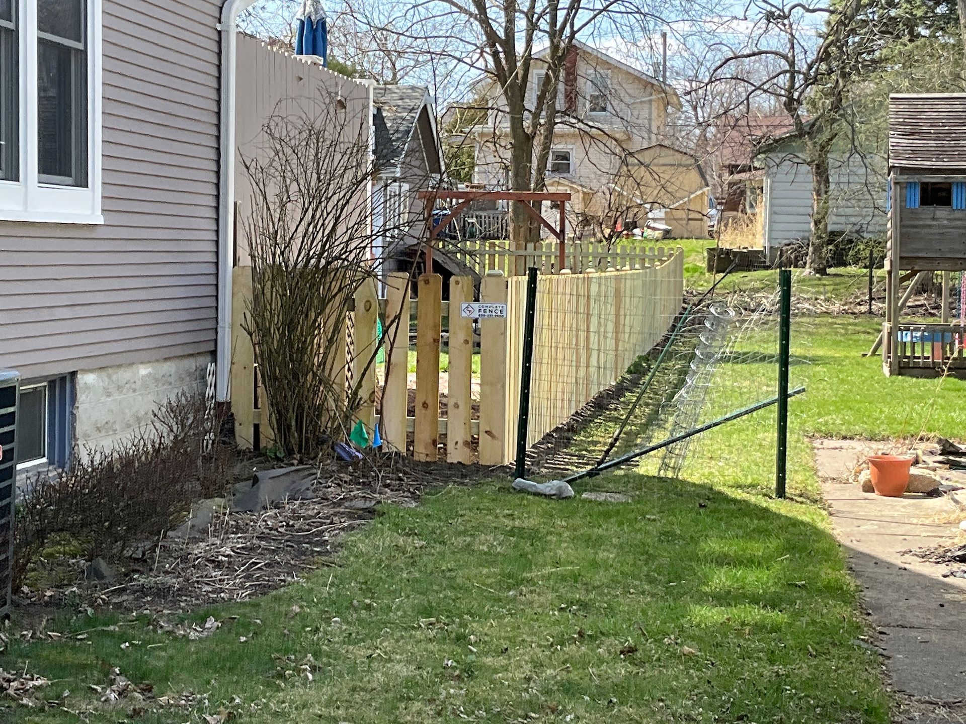 Backyard with a wooden fence and a chain-link fence, next to a house with a green lawn.