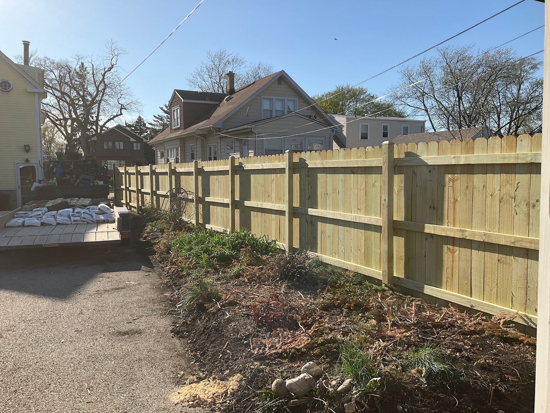 Wooden fence along a driveway with a house in the background on a sunny day.