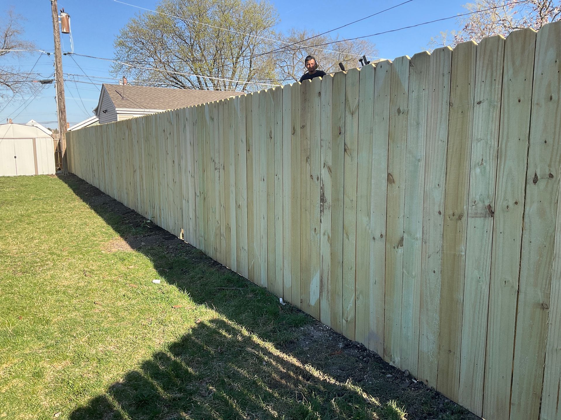 Wooden fence along green grass. Person atop fence in background. Sunny day.