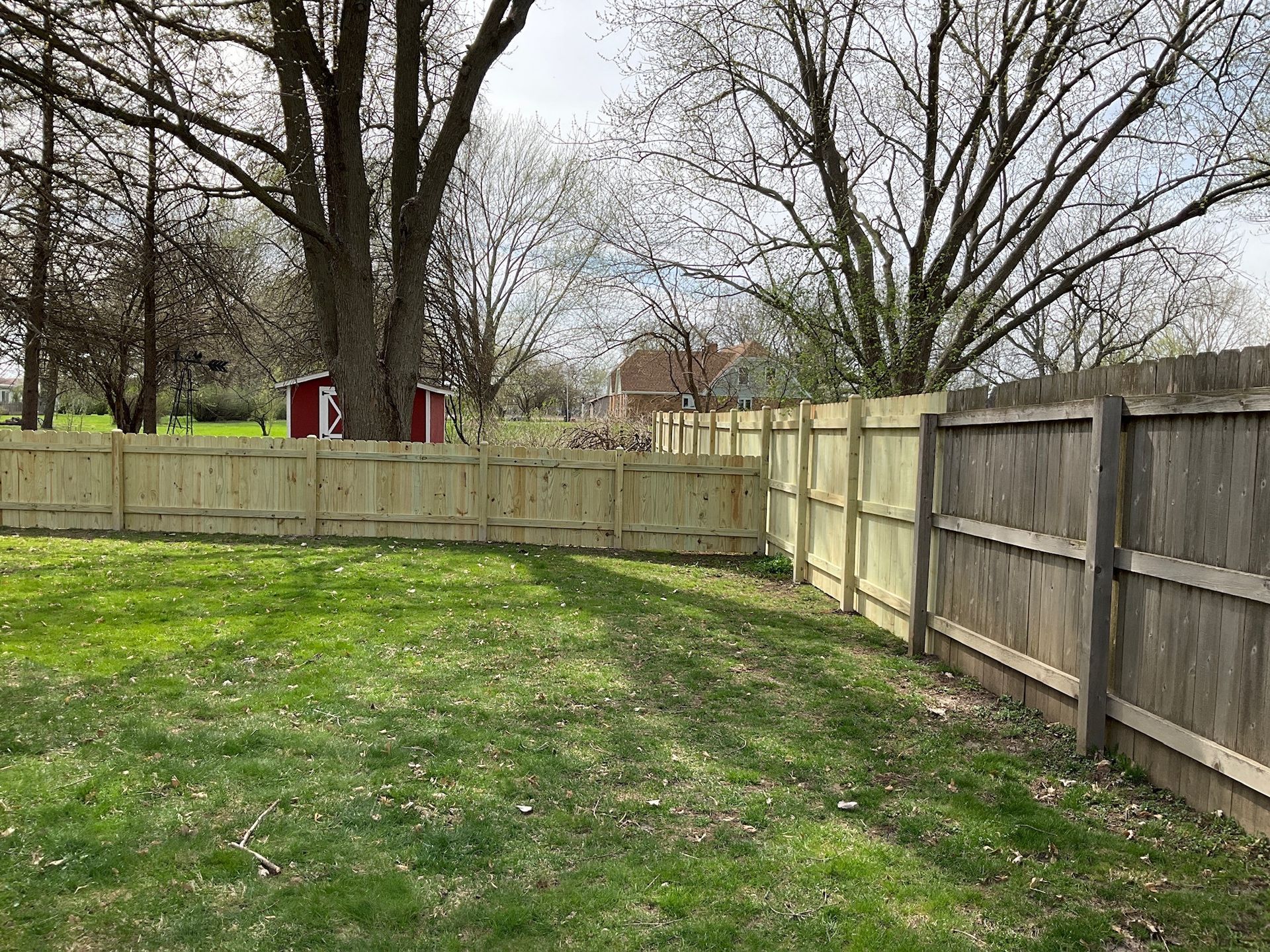 Grassy backyard with wooden fences and trees under a cloudy sky.