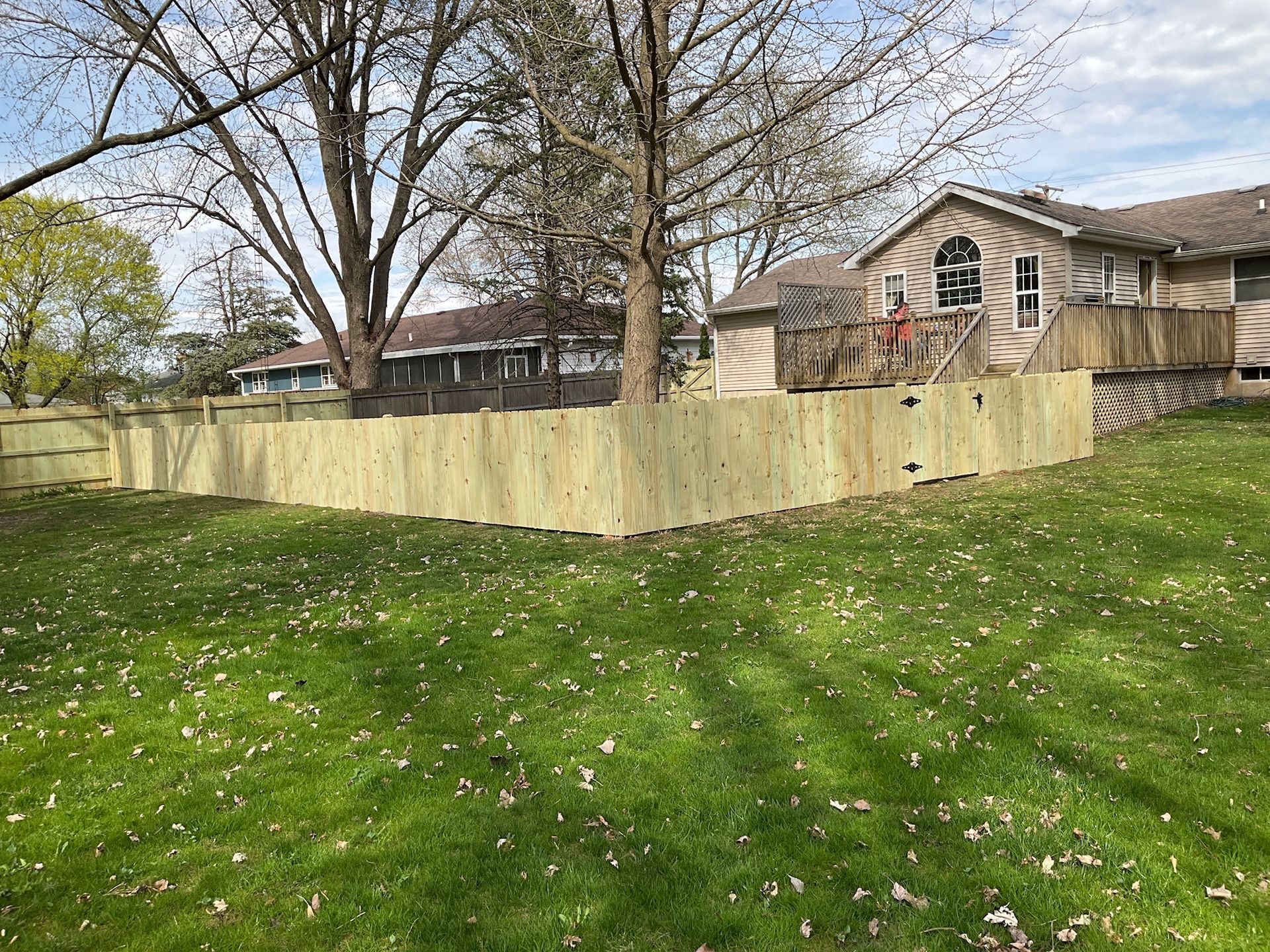 A new wooden fence surrounds a grassy backyard, adjacent to a house with a wooden deck.