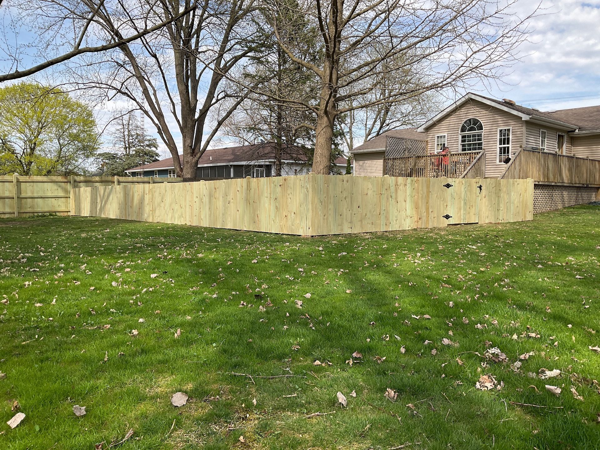 Wooden fence encloses a green lawn, houses in the background, trees overhead on a sunny day.
