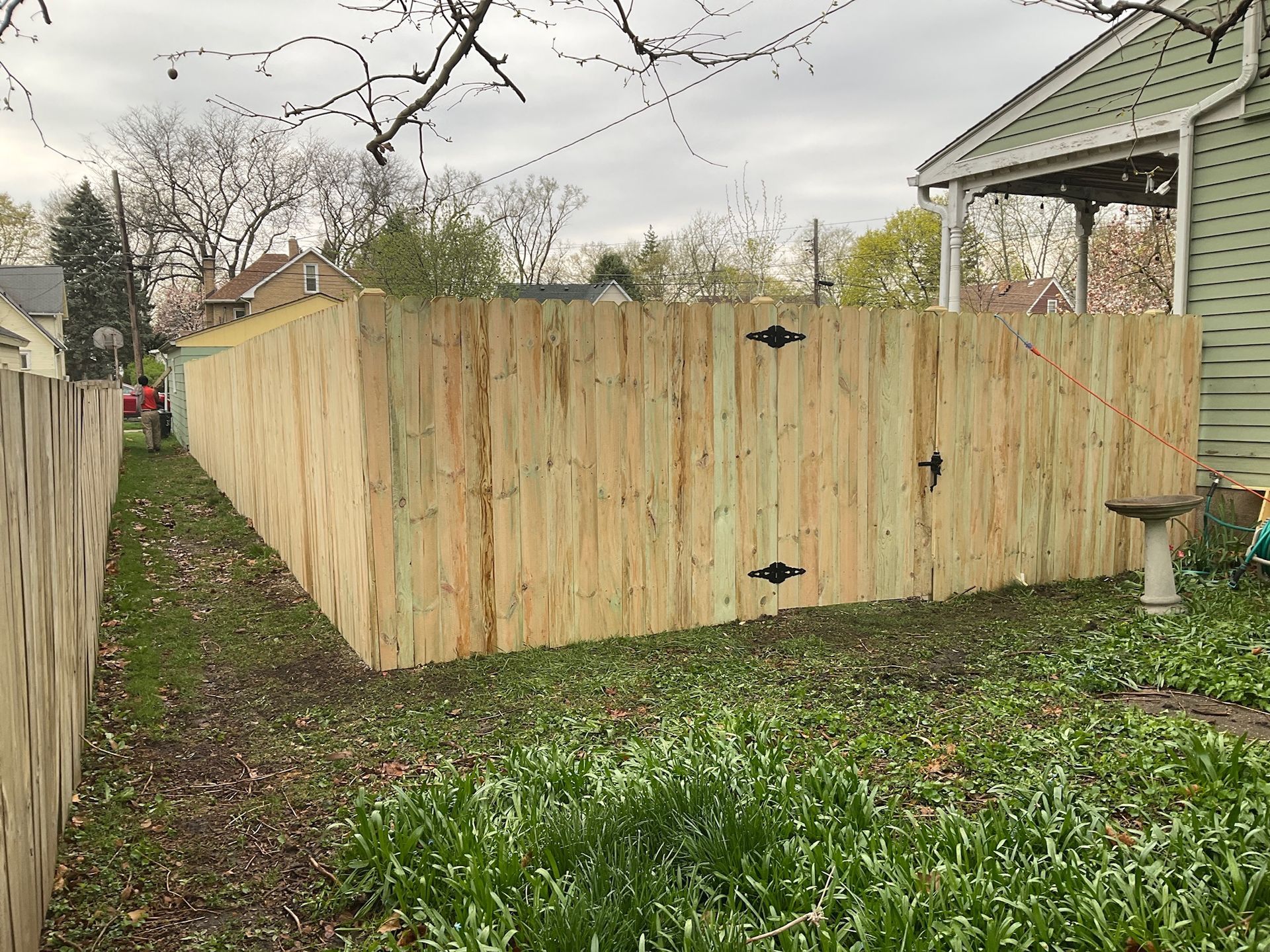 Wooden fence in a backyard, with a gate and birdbath.