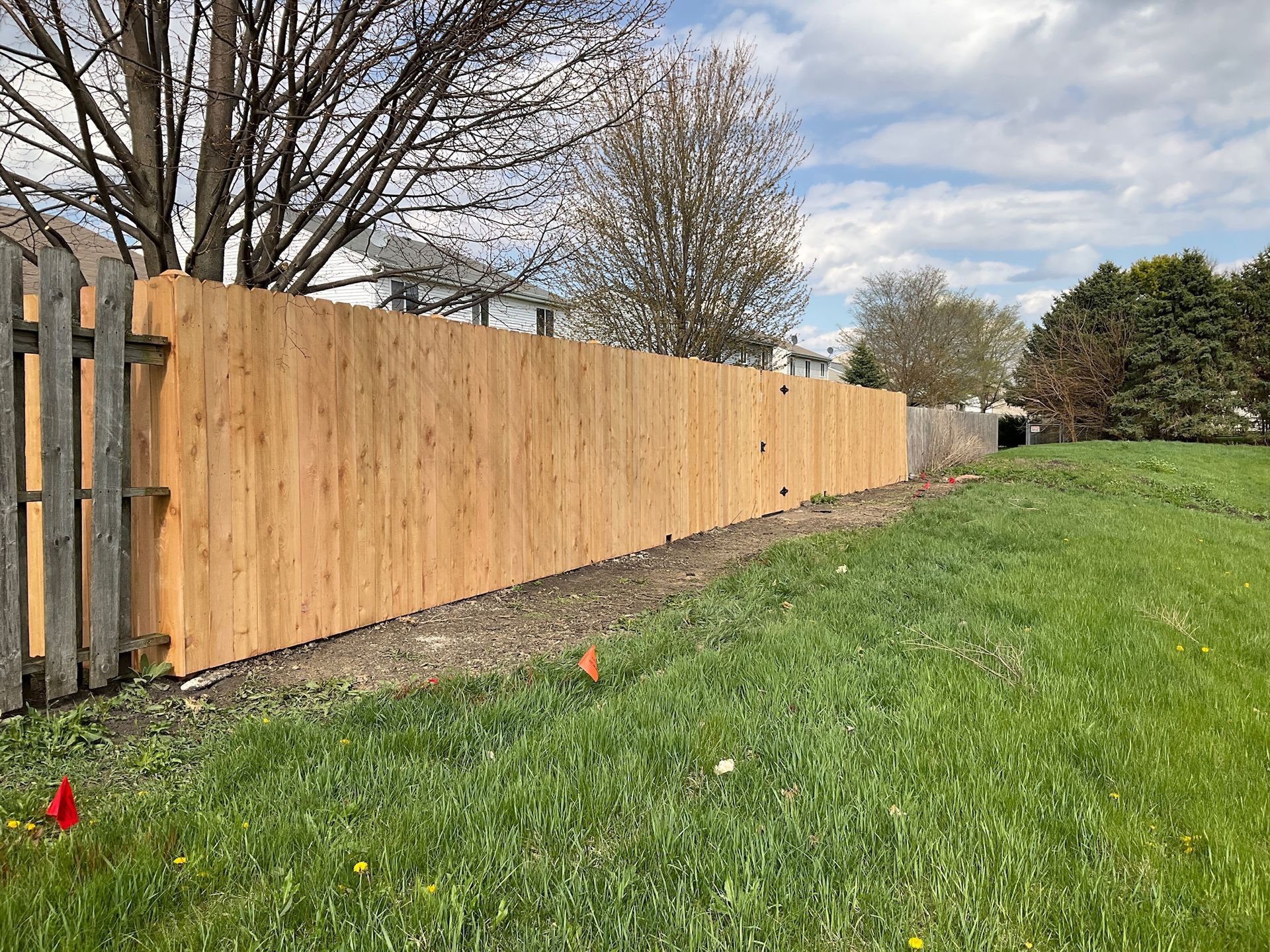 Wooden fence along grassy area, with trees and cloudy sky in background.