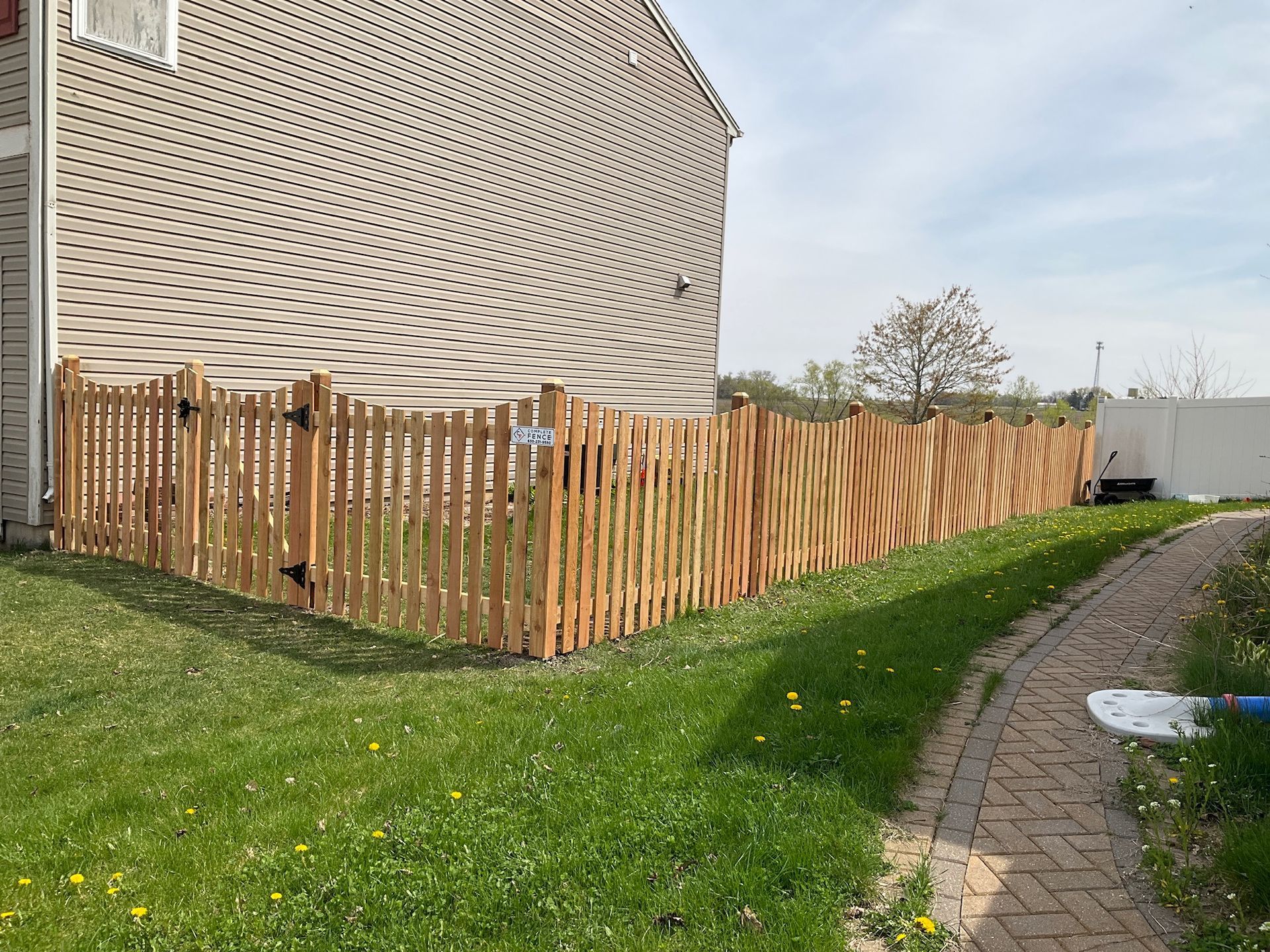 Wooden fence alongside a brick building and a green grassy lawn.