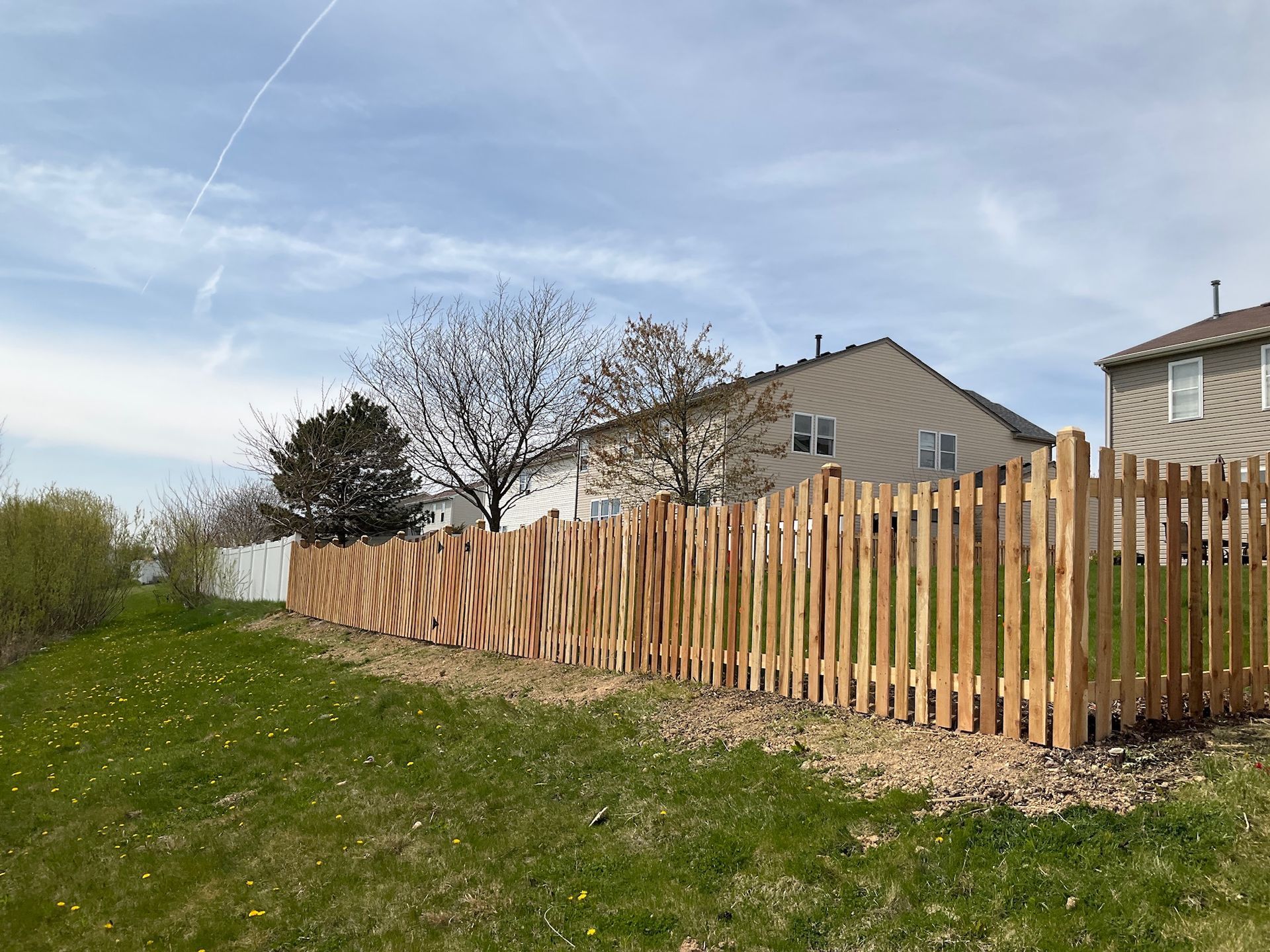Wooden fence in front of a house, set on a grassy hill, under a cloudy sky.