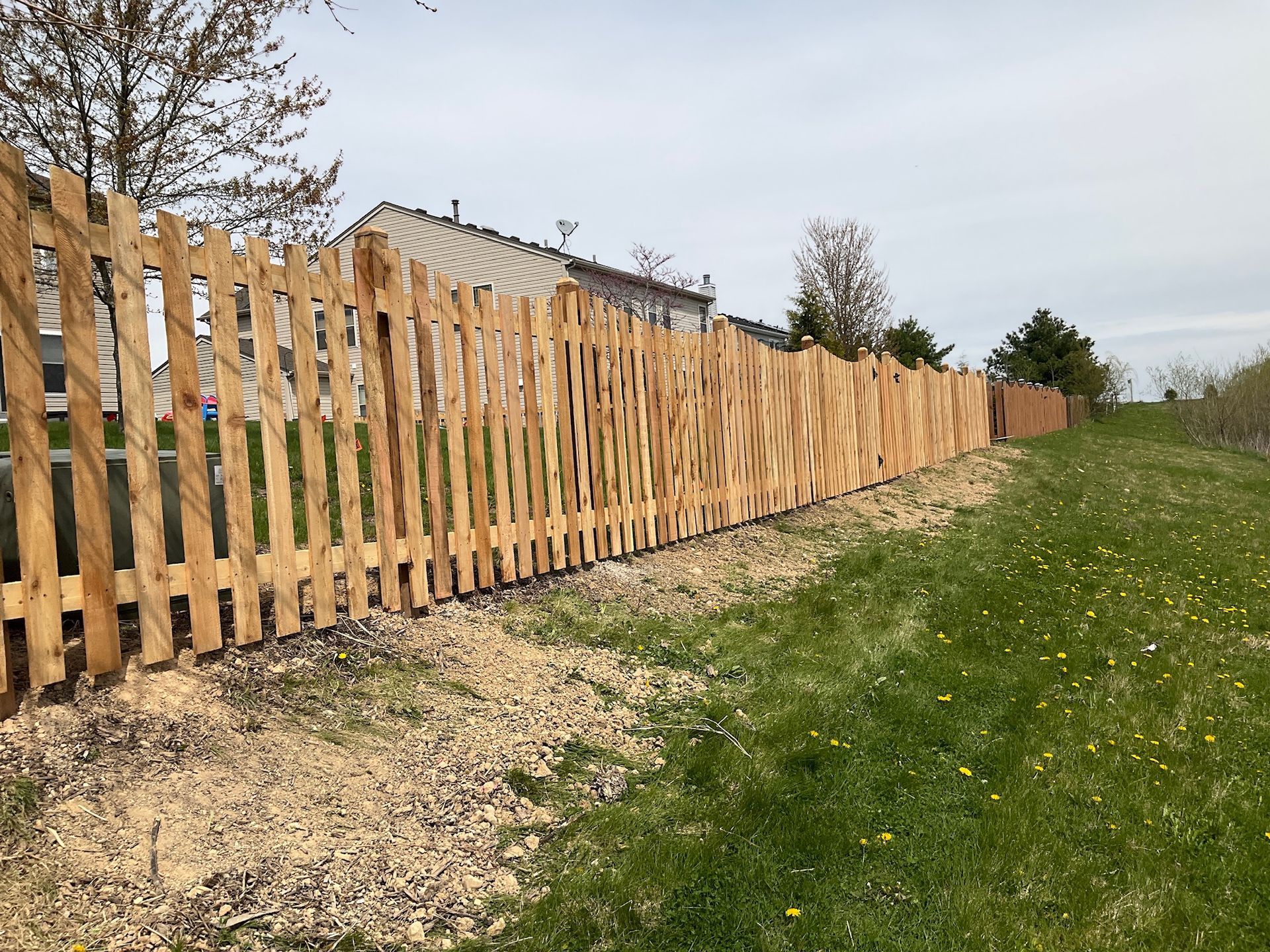 Wooden zigzag fence along grassy slope with residential buildings in the background.
