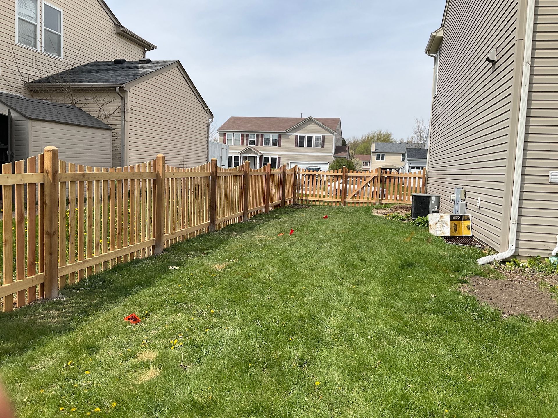 Backyard with newly built wooden fence, grass, and houses.