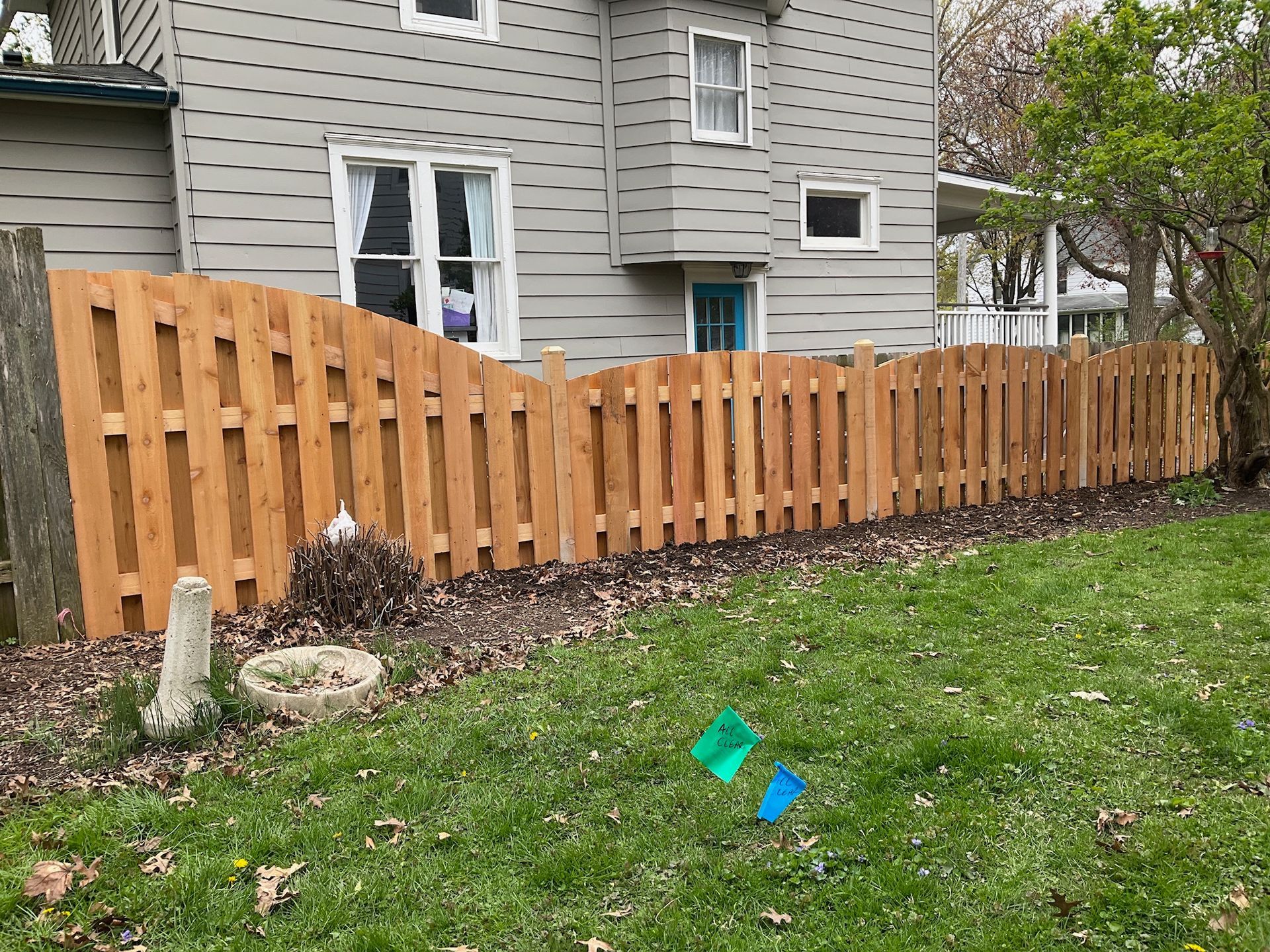 Wooden fence in front of a gray house, on a grassy lawn.