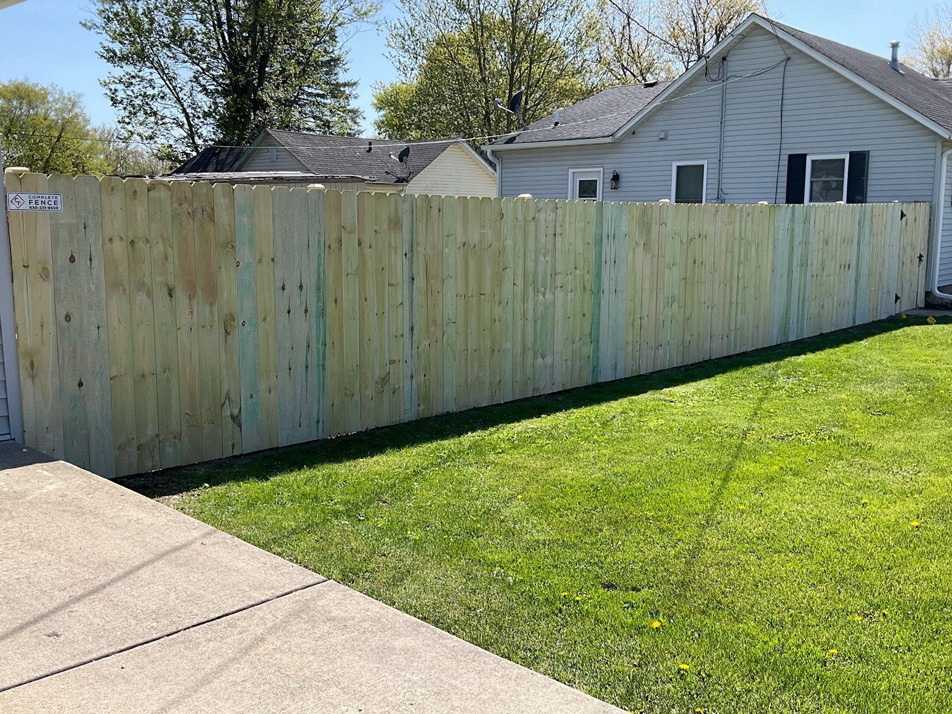 A wooden fence surrounding a grassy yard with a house in the background.
