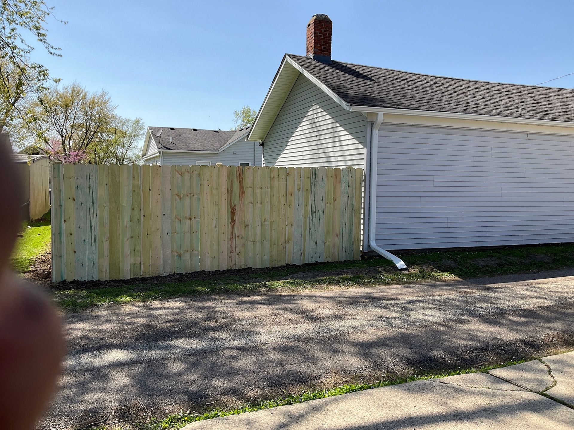 Wooden fence next to a white building and a gravel driveway on a sunny day.