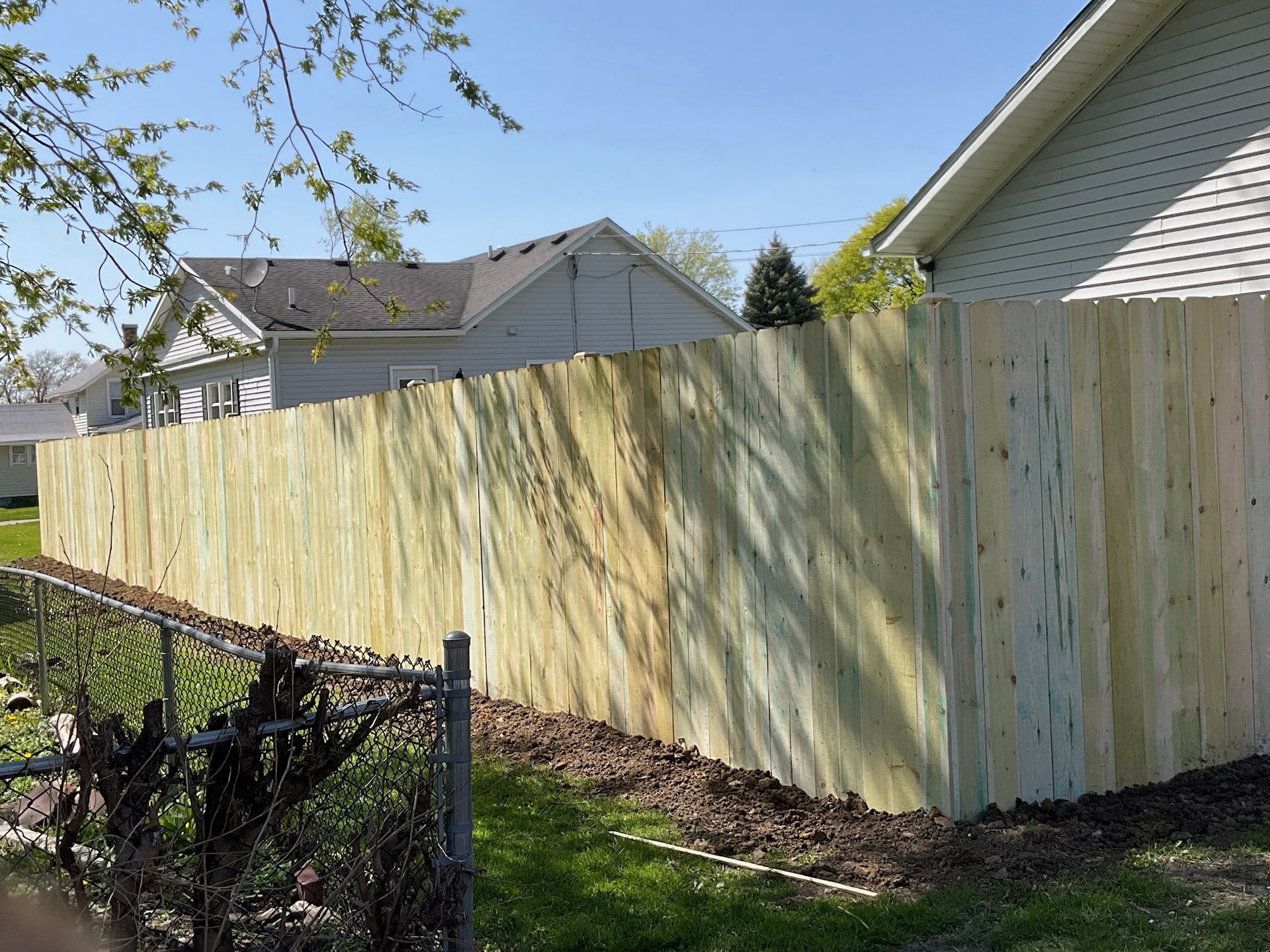 Wooden fence bordering a yard, with houses in the background on a sunny day.