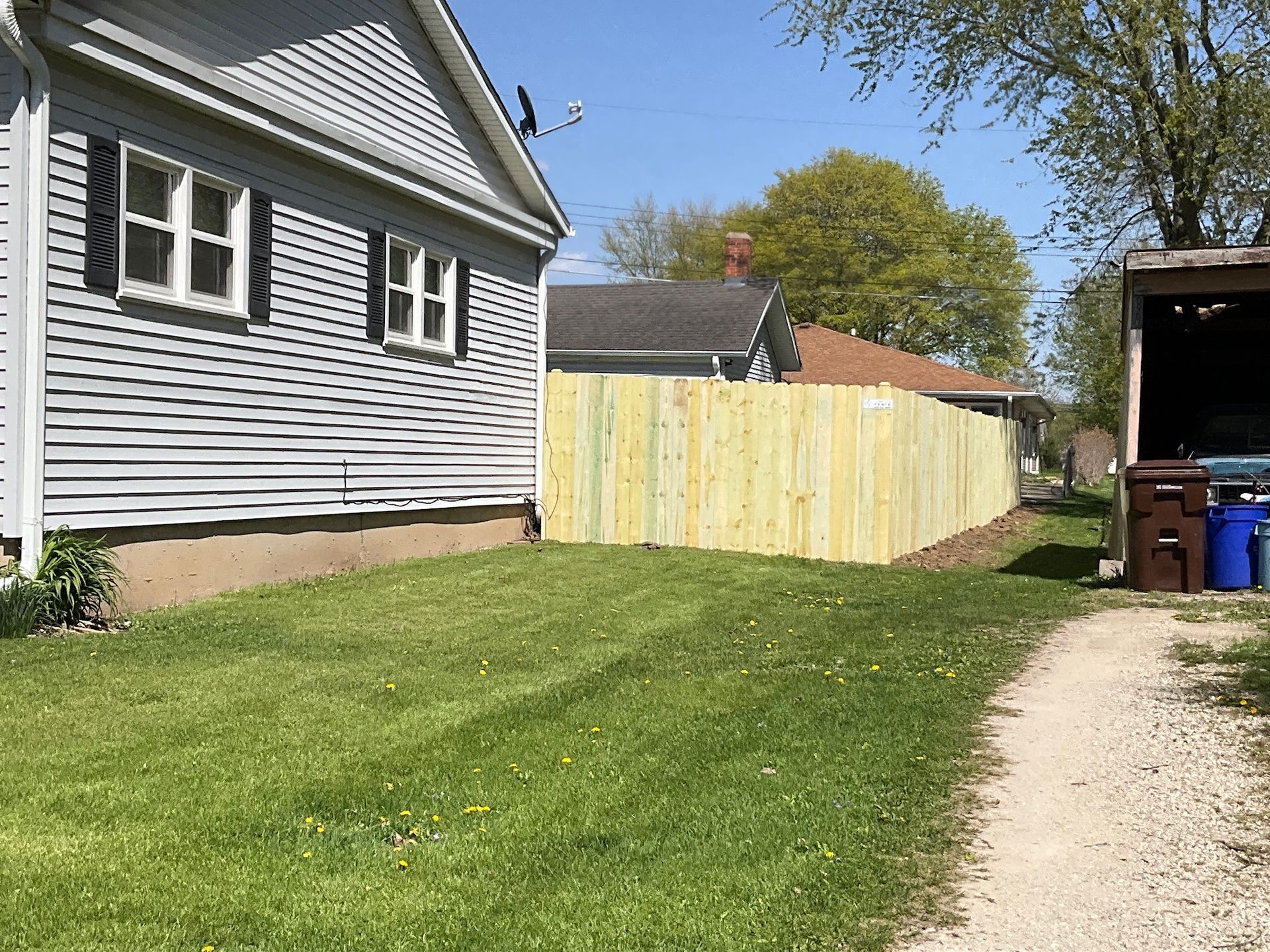 Wooden fence separating yards next to a house with gray siding and green lawn.
