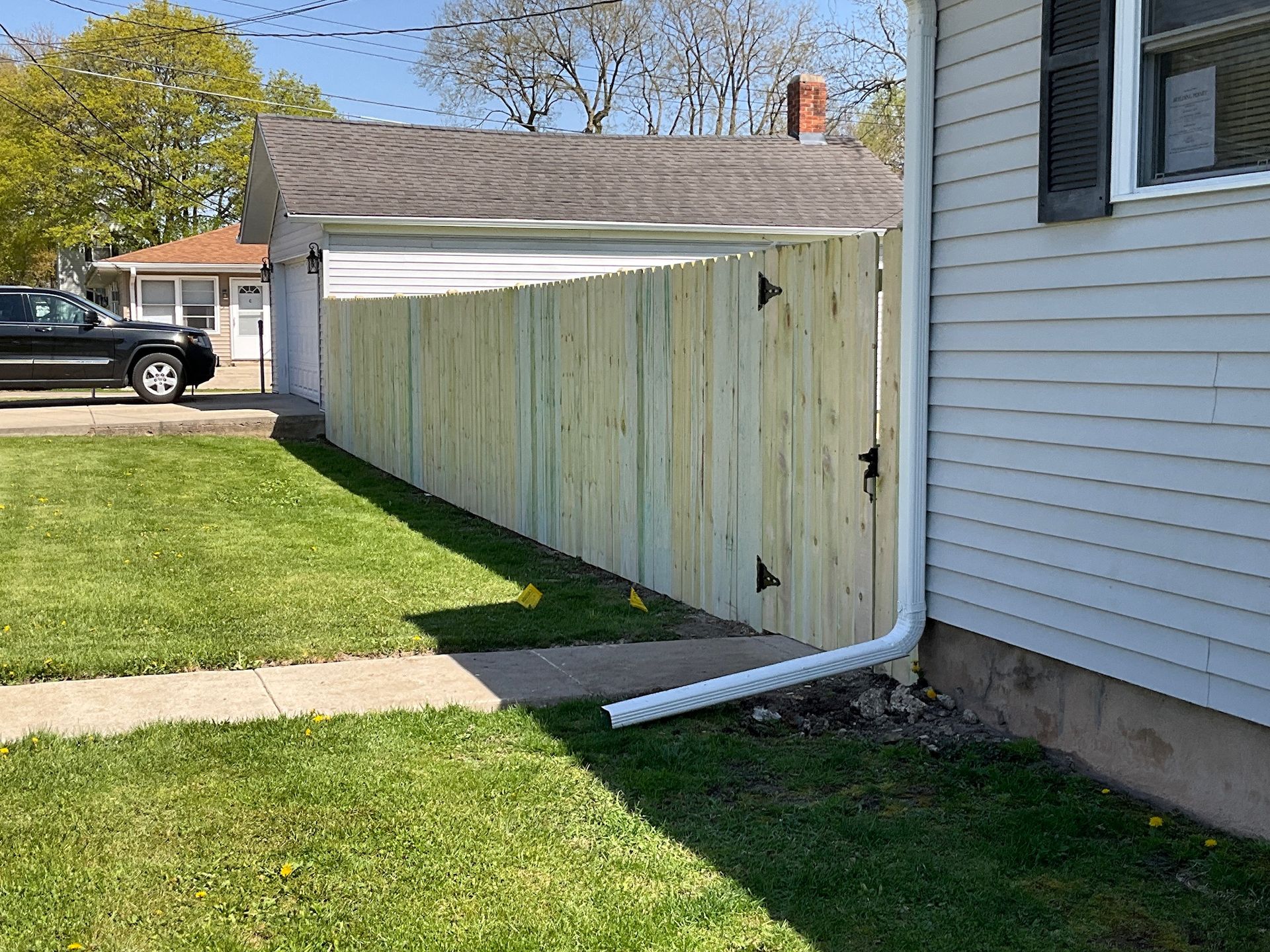 Wooden fence along a house, with grass in front and car parked nearby.