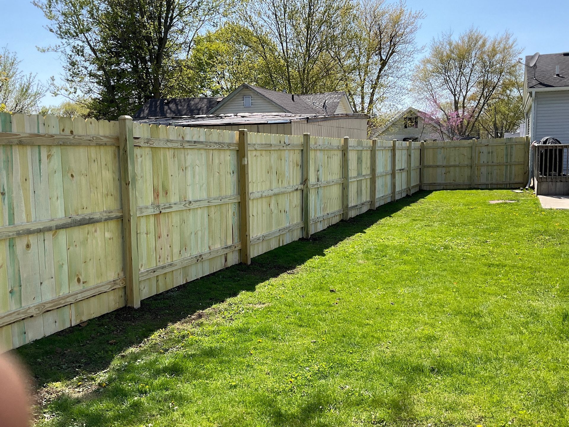 Wooden fence in a backyard with green grass under a clear blue sky.