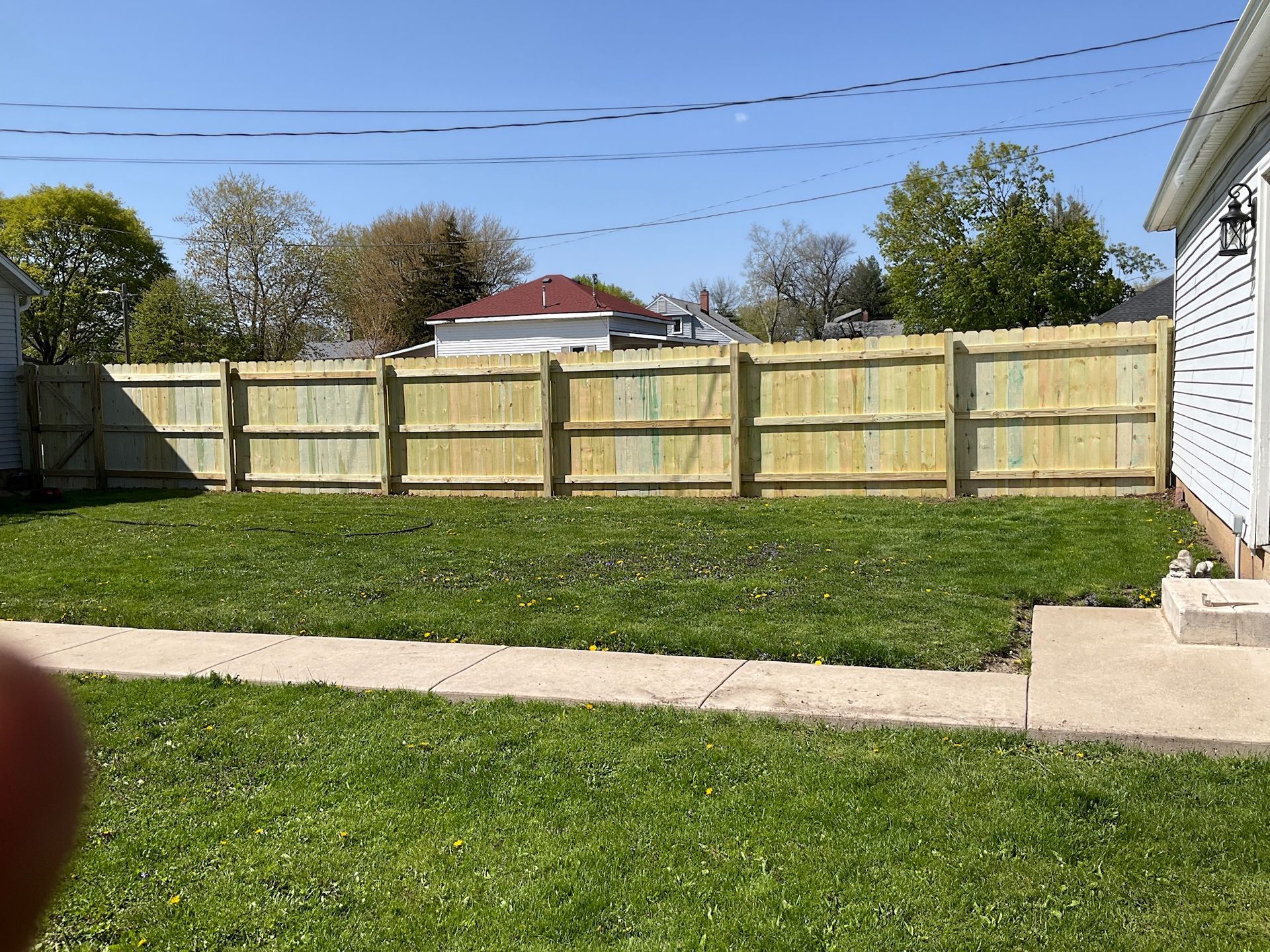 Wooden fence in a backyard, with green grass and a house to the right.