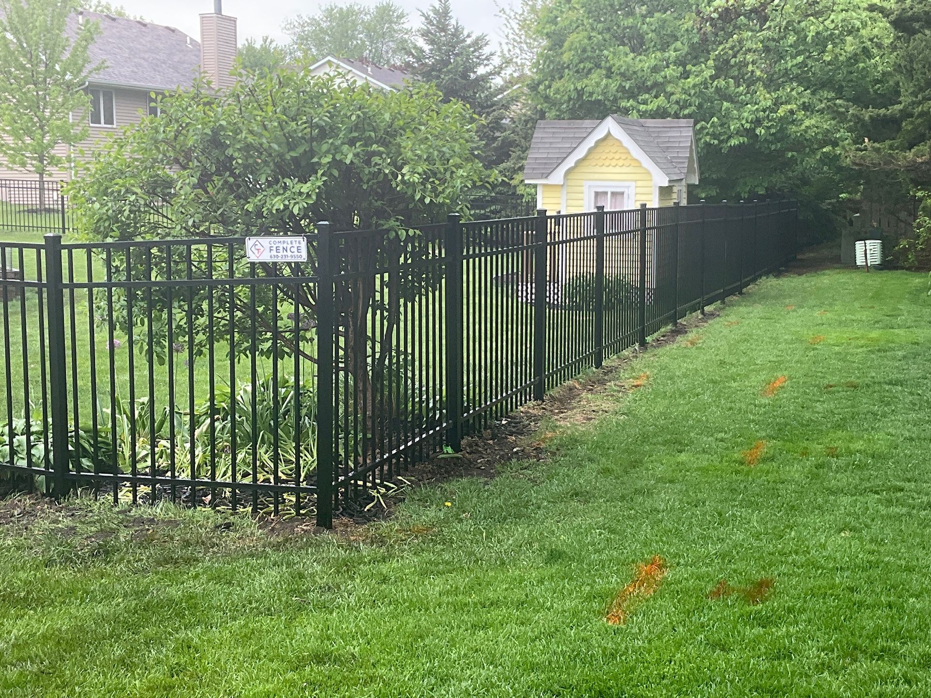 Black metal fence in a green yard, with a yellow shed in the background.