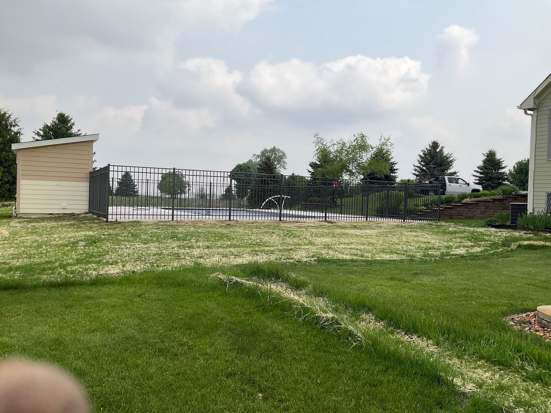 Backyard with a swimming pool, shed, and green grass under a cloudy sky.