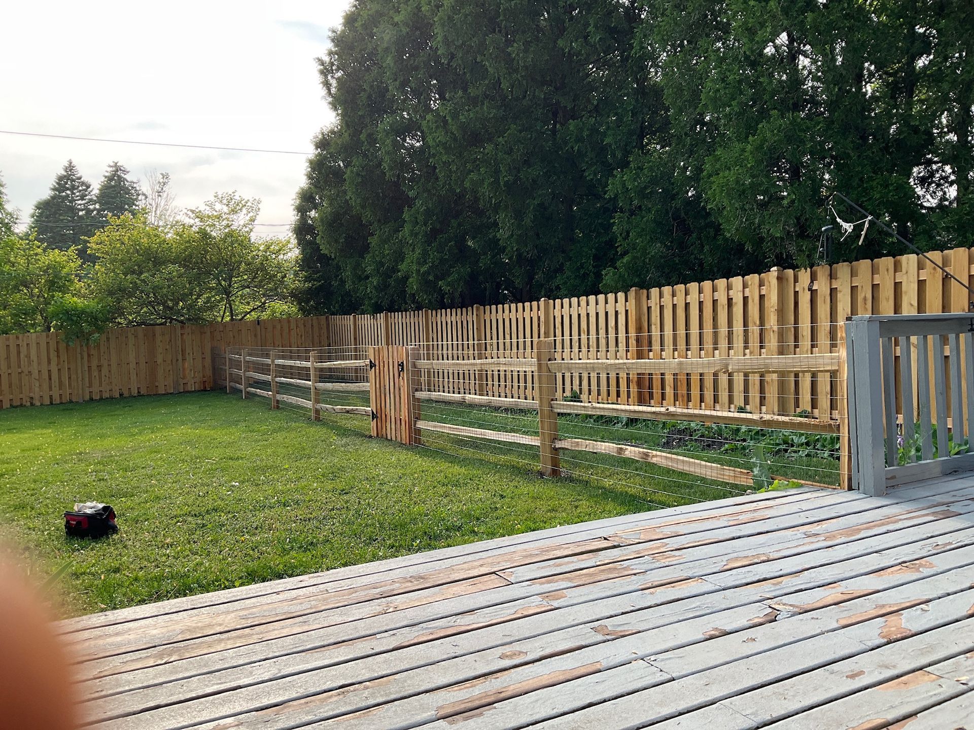 A backyard with a wooden fence and a lawn. A deck is in the foreground.