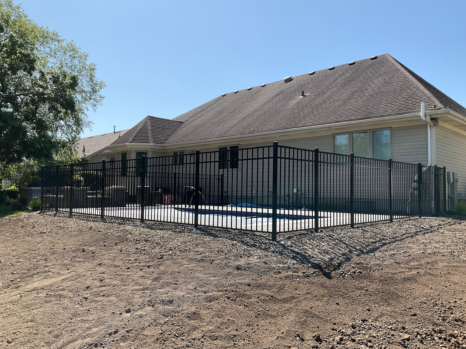 Black fence surrounds a concrete patio near a house with a brown roof and clear sky.