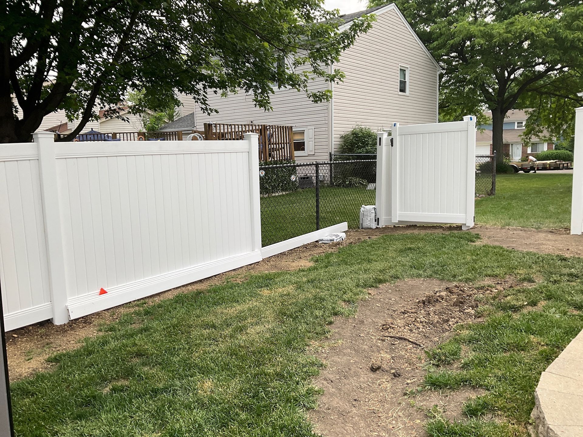 White vinyl fence with gate in a backyard, grass and trees in view.