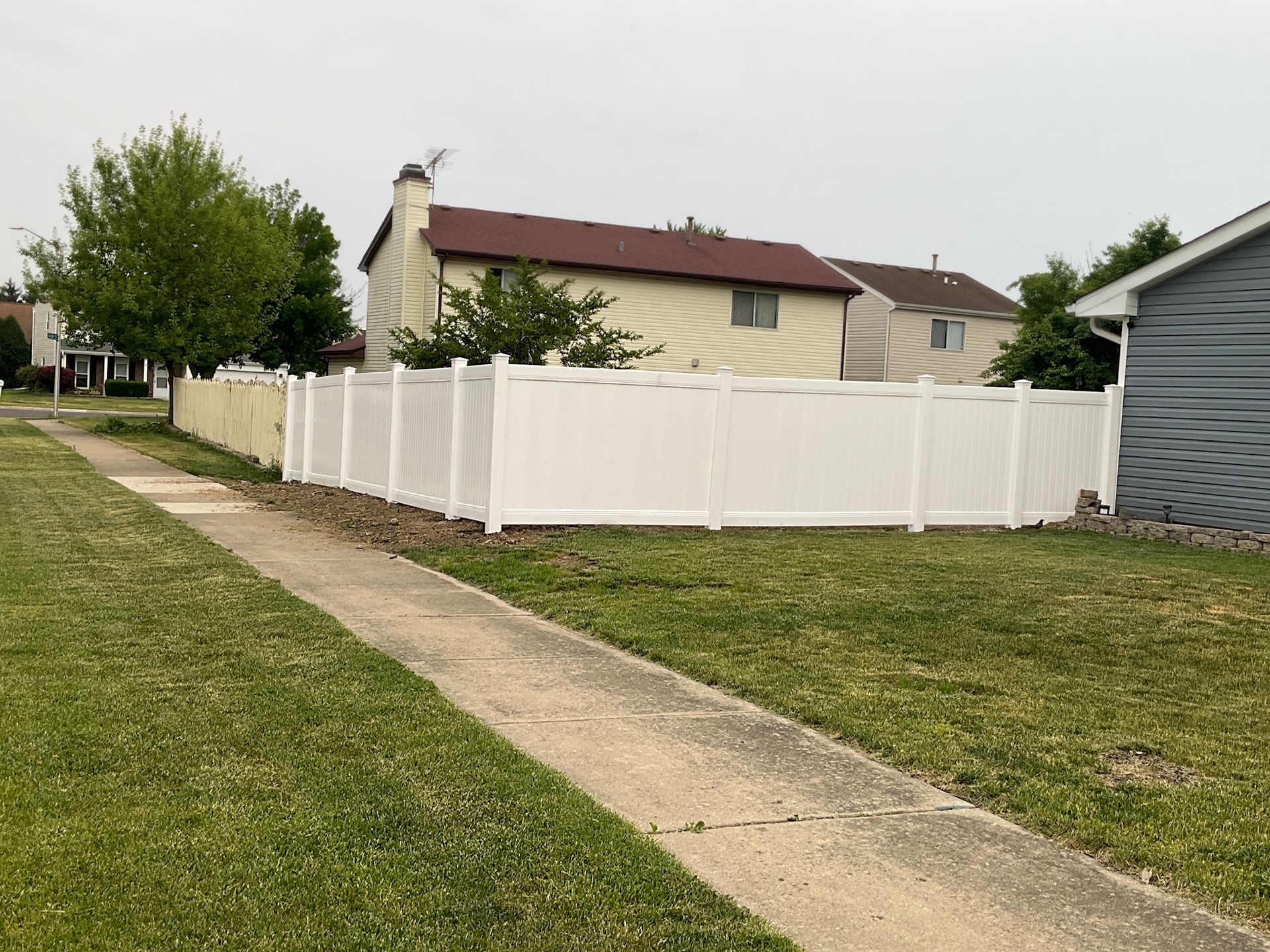 White vinyl fence bordering a residential property, sidewalk in foreground.