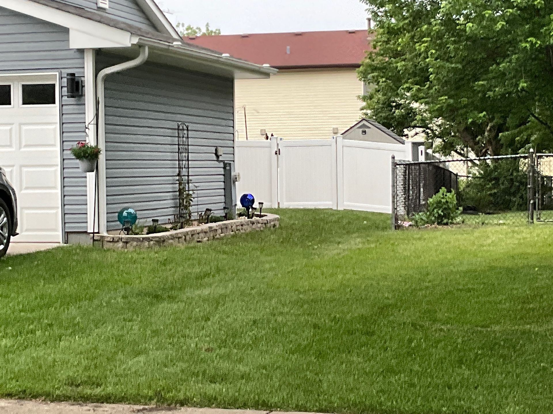 Blue house with white garage door and white fence; green lawn and landscaping.