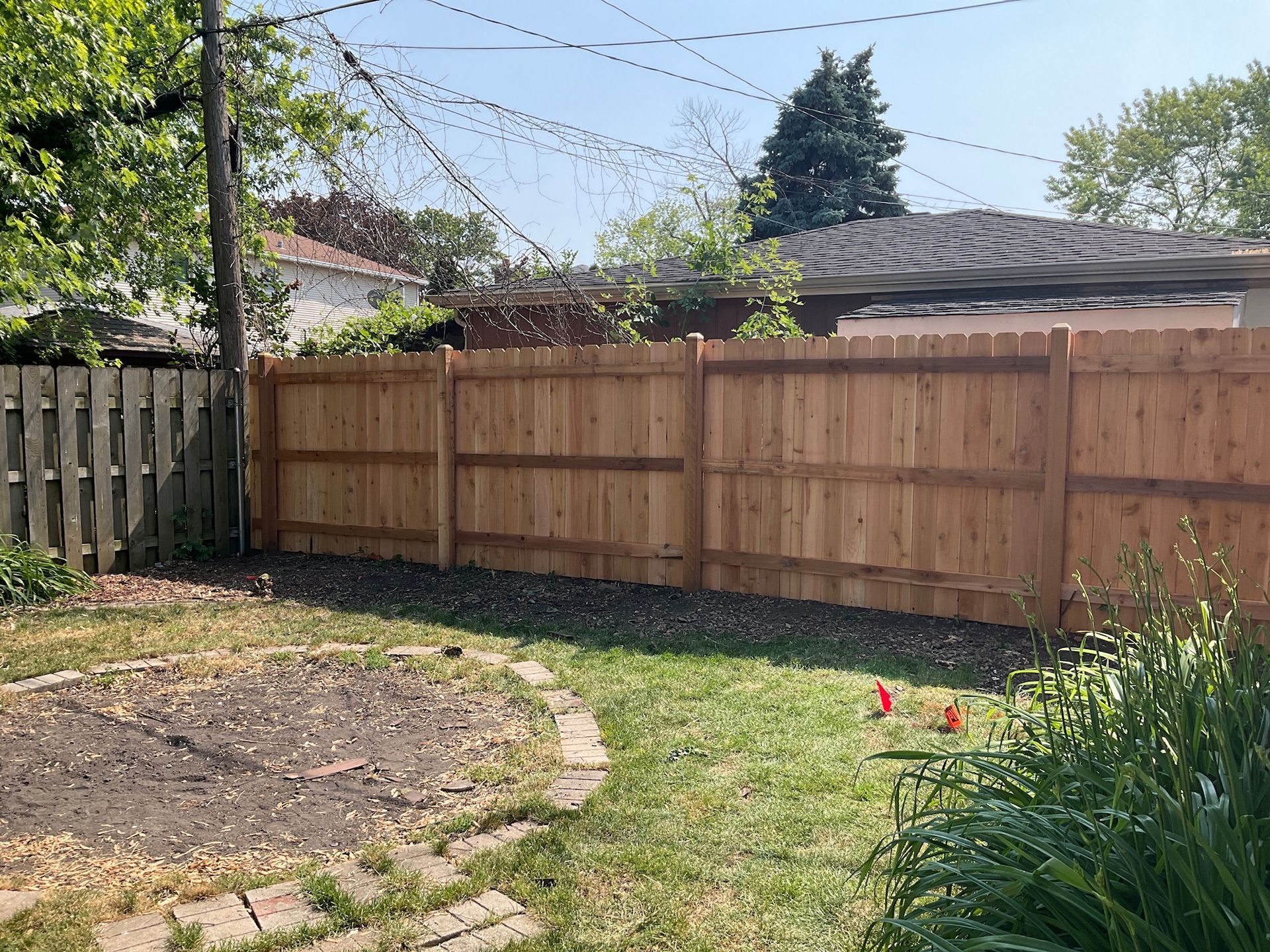 Backyard with a wooden fence. Darker, older fence on the left; newer, lighter fence on the right. Green grass and blue sky.