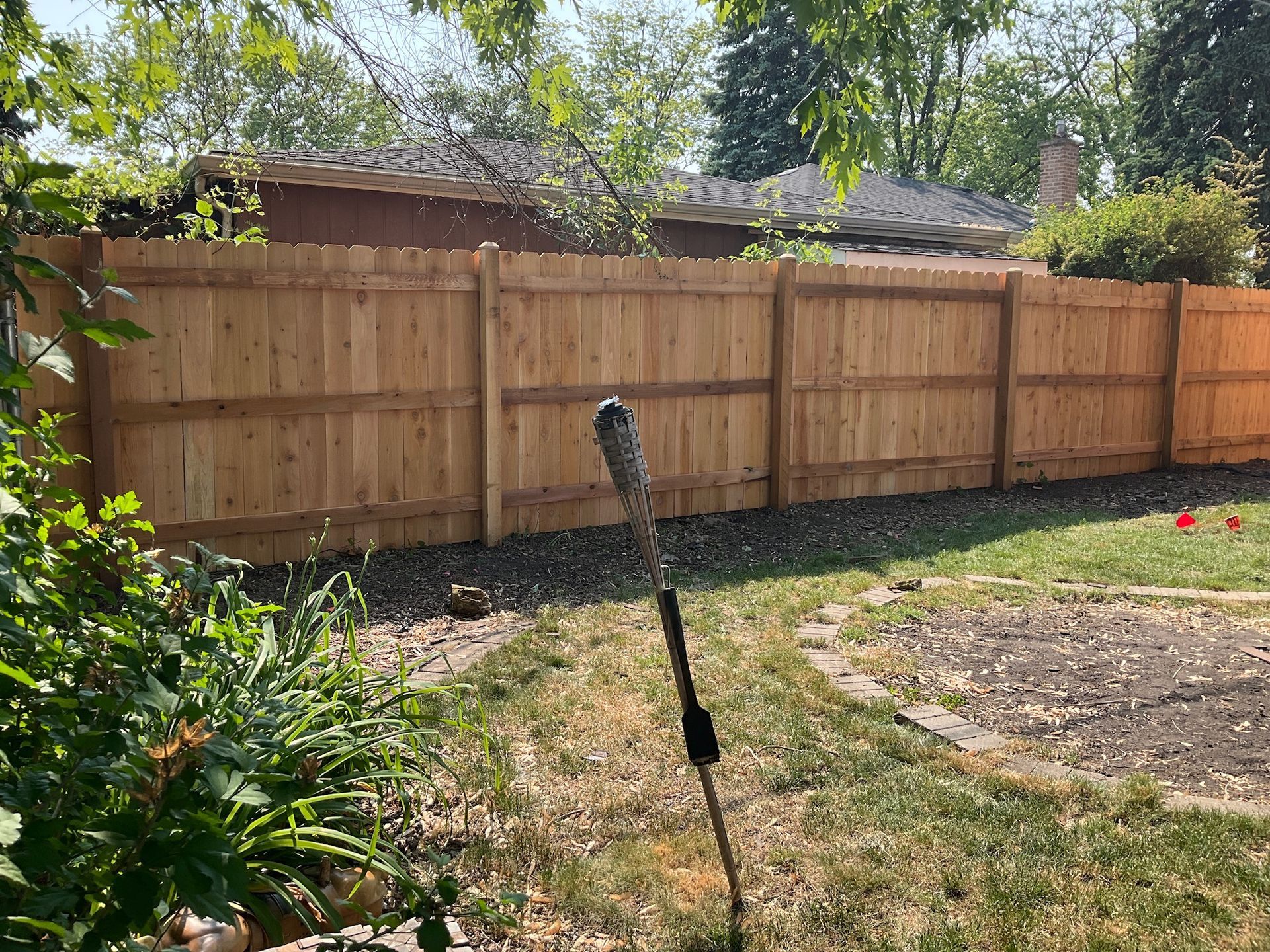 Wooden fence in a backyard, with a hose in front of it and a house in the background.