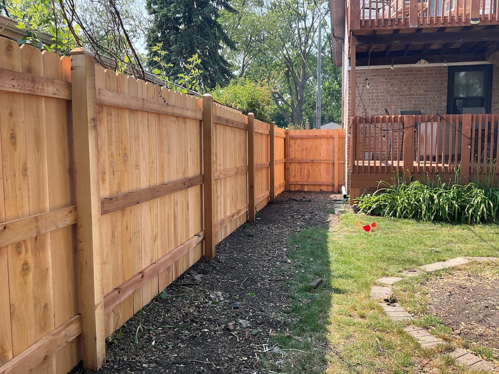 Wooden fence alongside a building. Brown planks, gravel path, and grass visible.