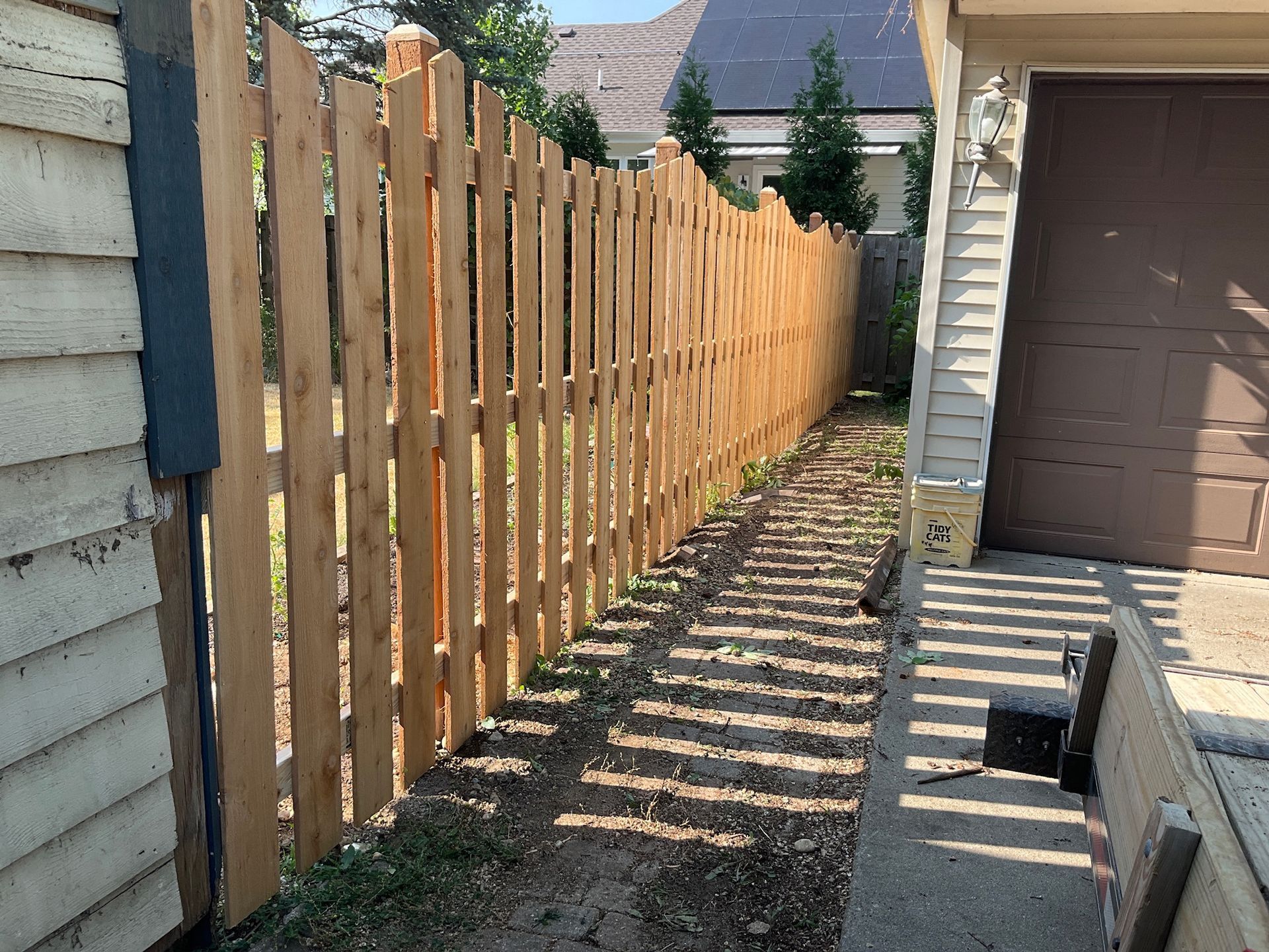Wooden fence along a narrow pathway between a house and garage.