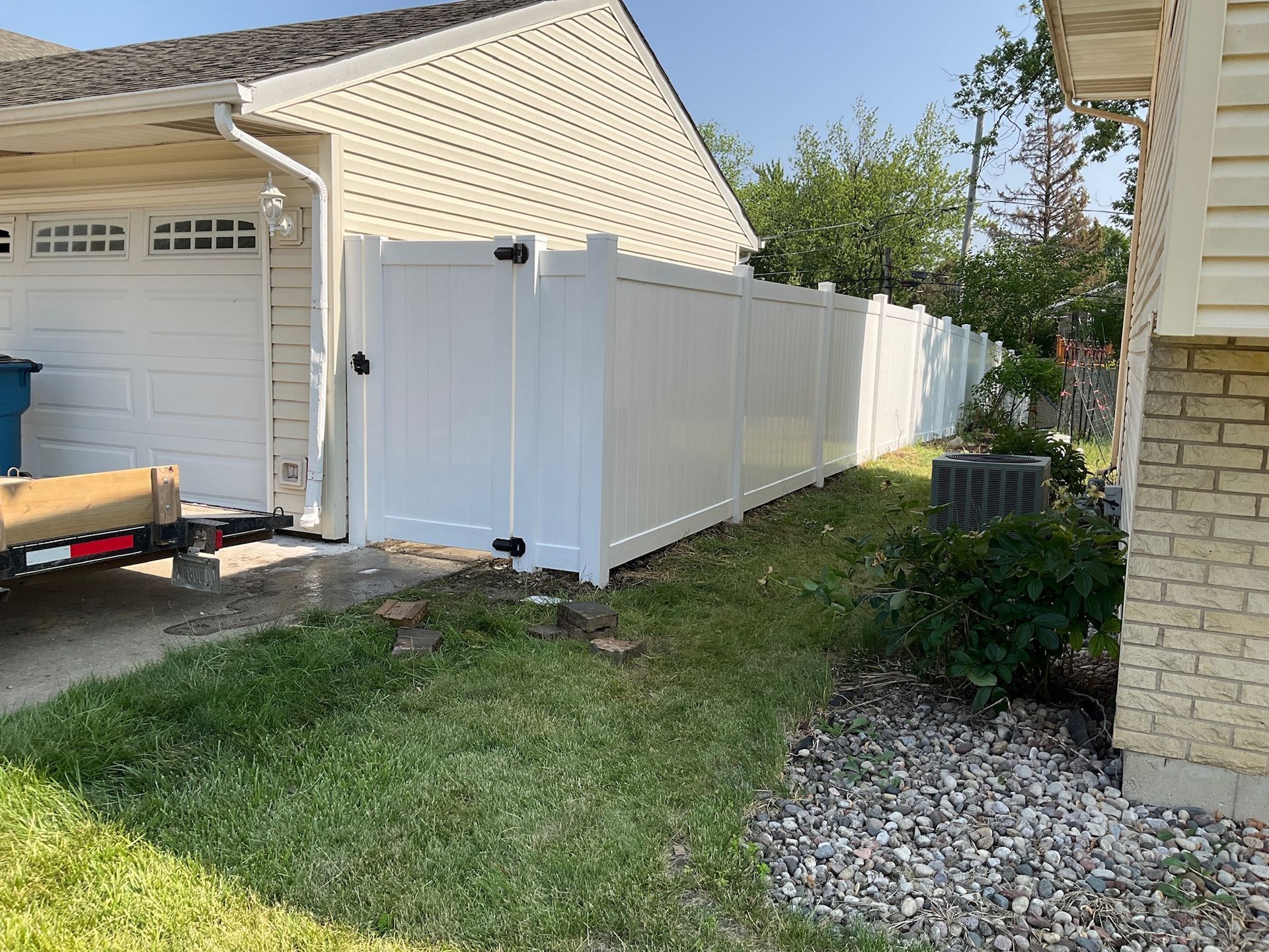 White vinyl fence with gate alongside a garage and house on a grassy area.