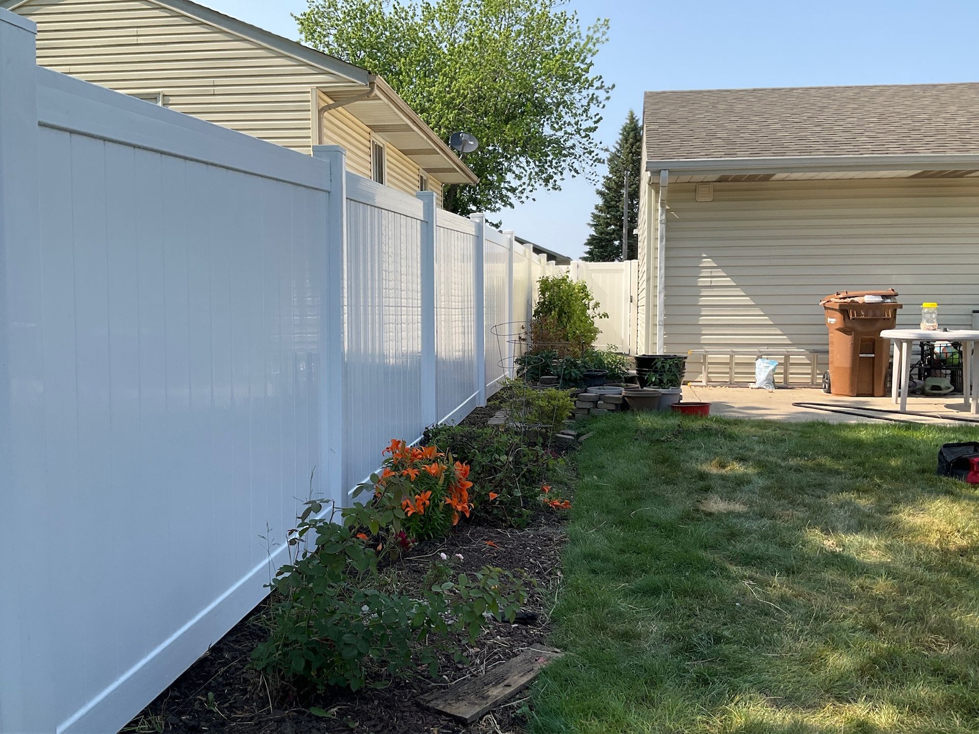 White vinyl fence alongside a yard with a garden bed, house, and garage.