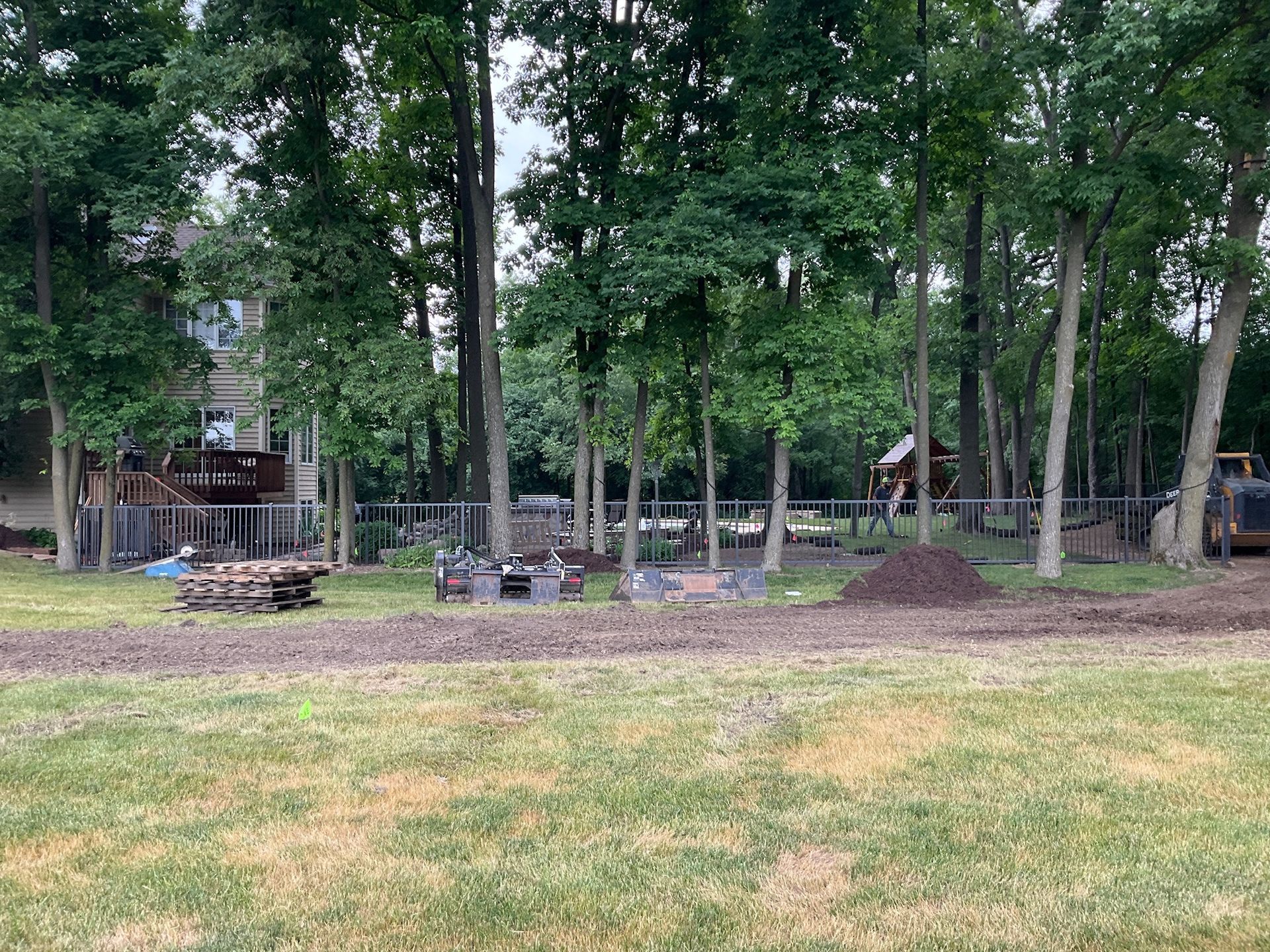A backyard scene with trees, a fence, a house, and construction materials.