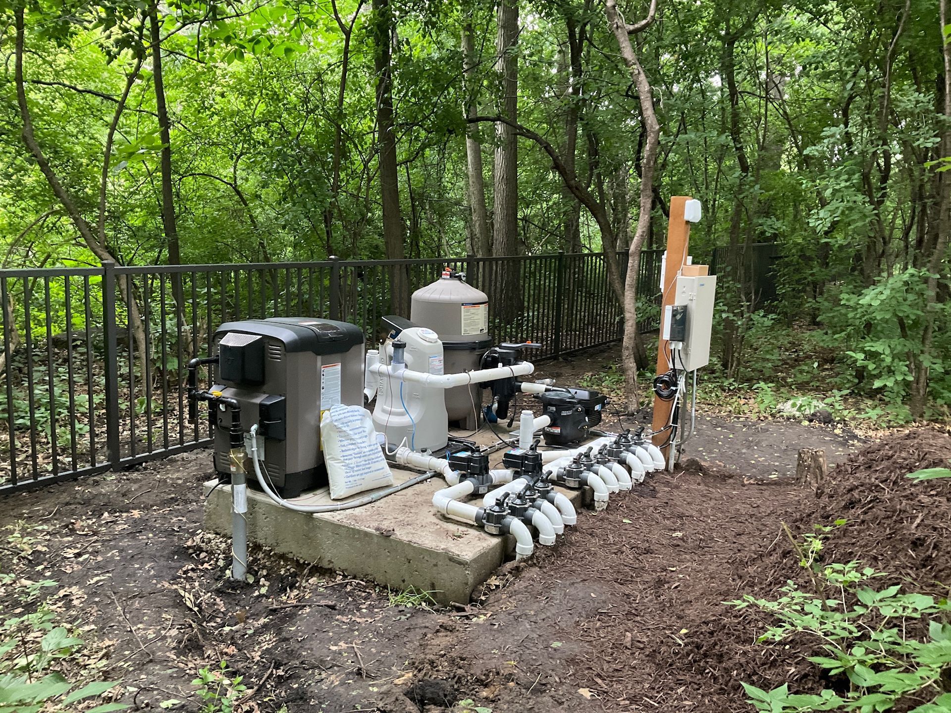 Pool equipment enclosure in wooded area with fence.